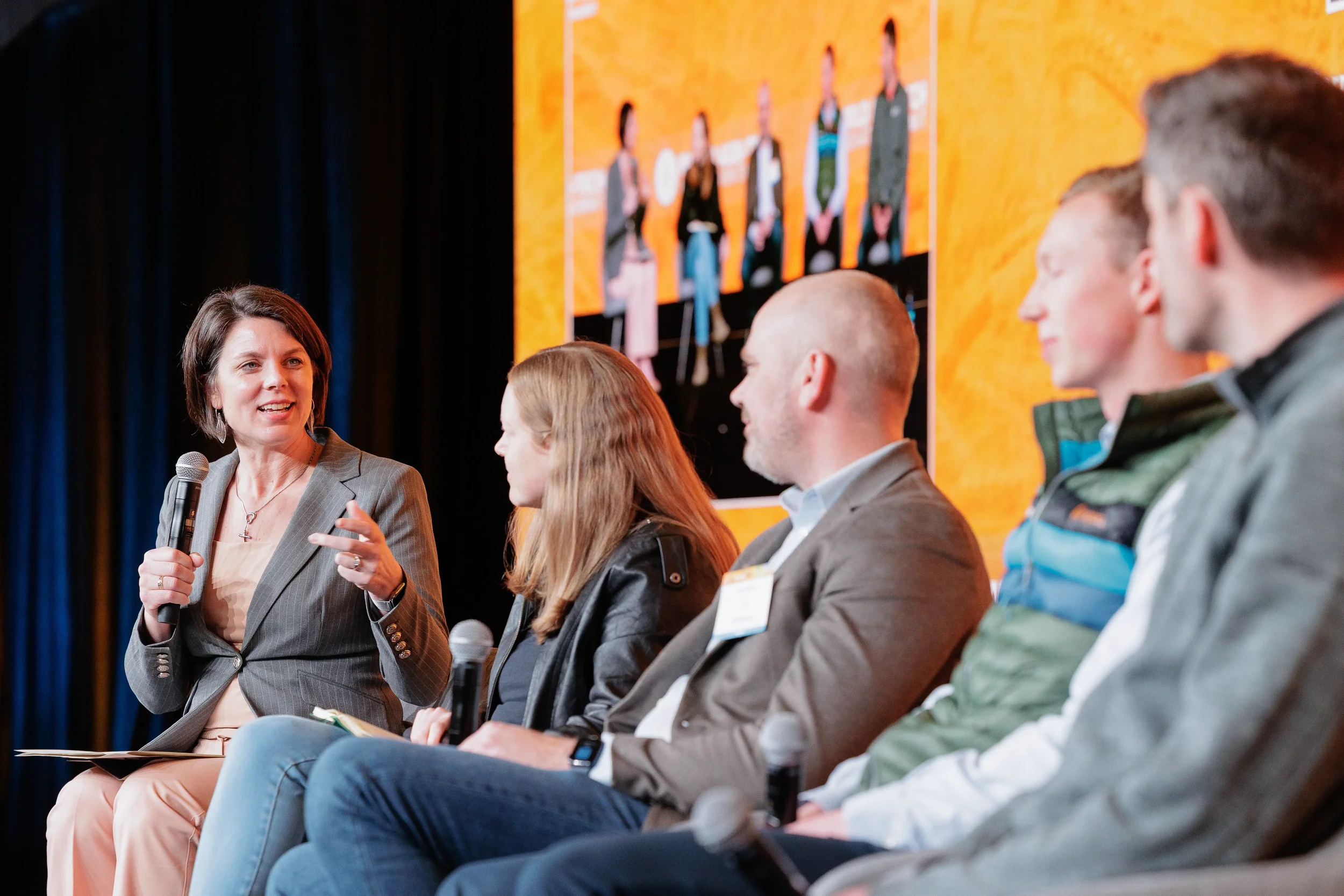 Moderator with microphone leads panel of four seated speakers on stage at Chicago corporate conference