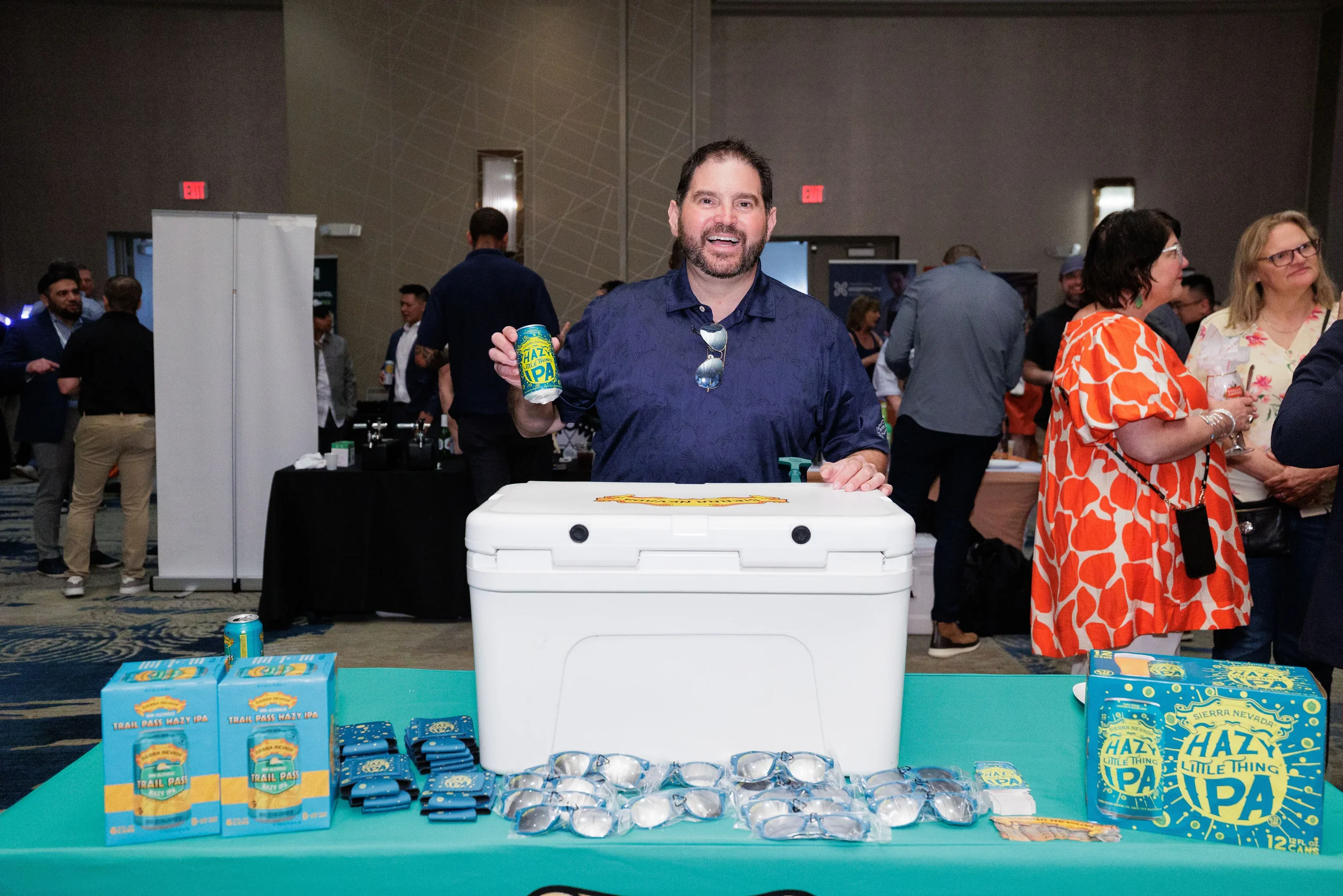 Smiling booth staff holds up branded can beside cooler and giveaways at Orlando corporate trade show