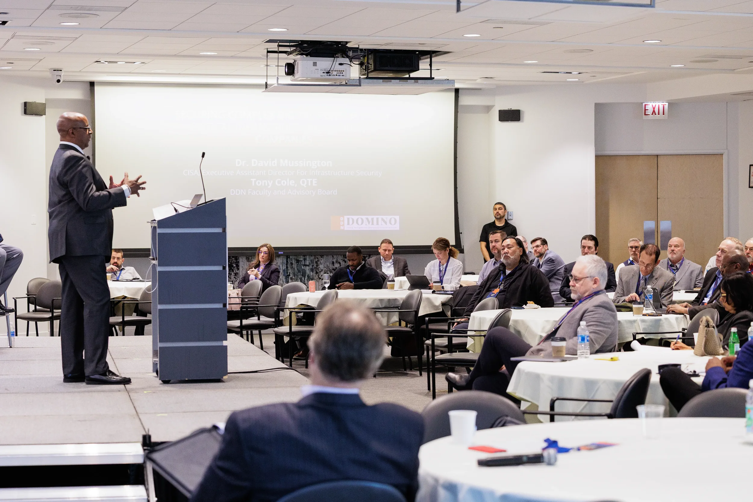 Speaker gestures at podium on stage before full seated audience at Orlando industry conference