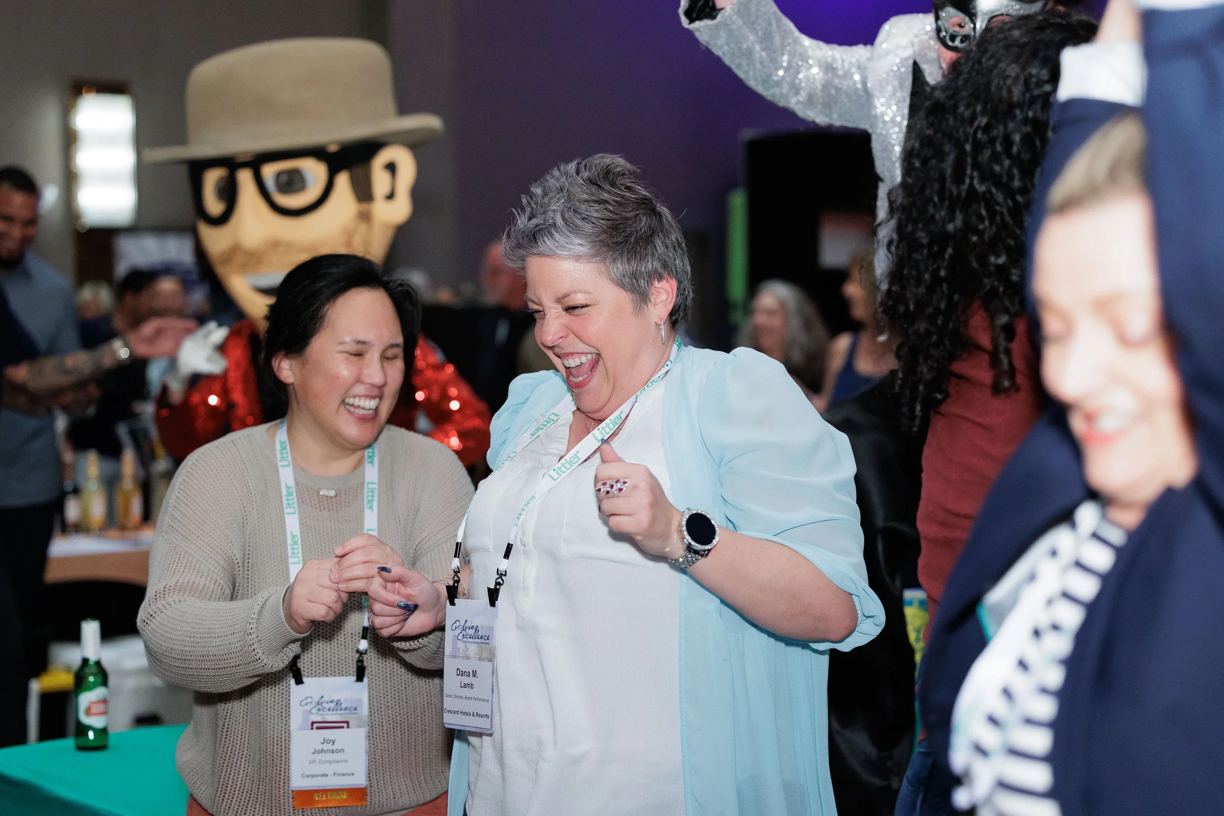 Two attendees with lanyards laugh together near mascot character at Chicago corporate conference expo reception
