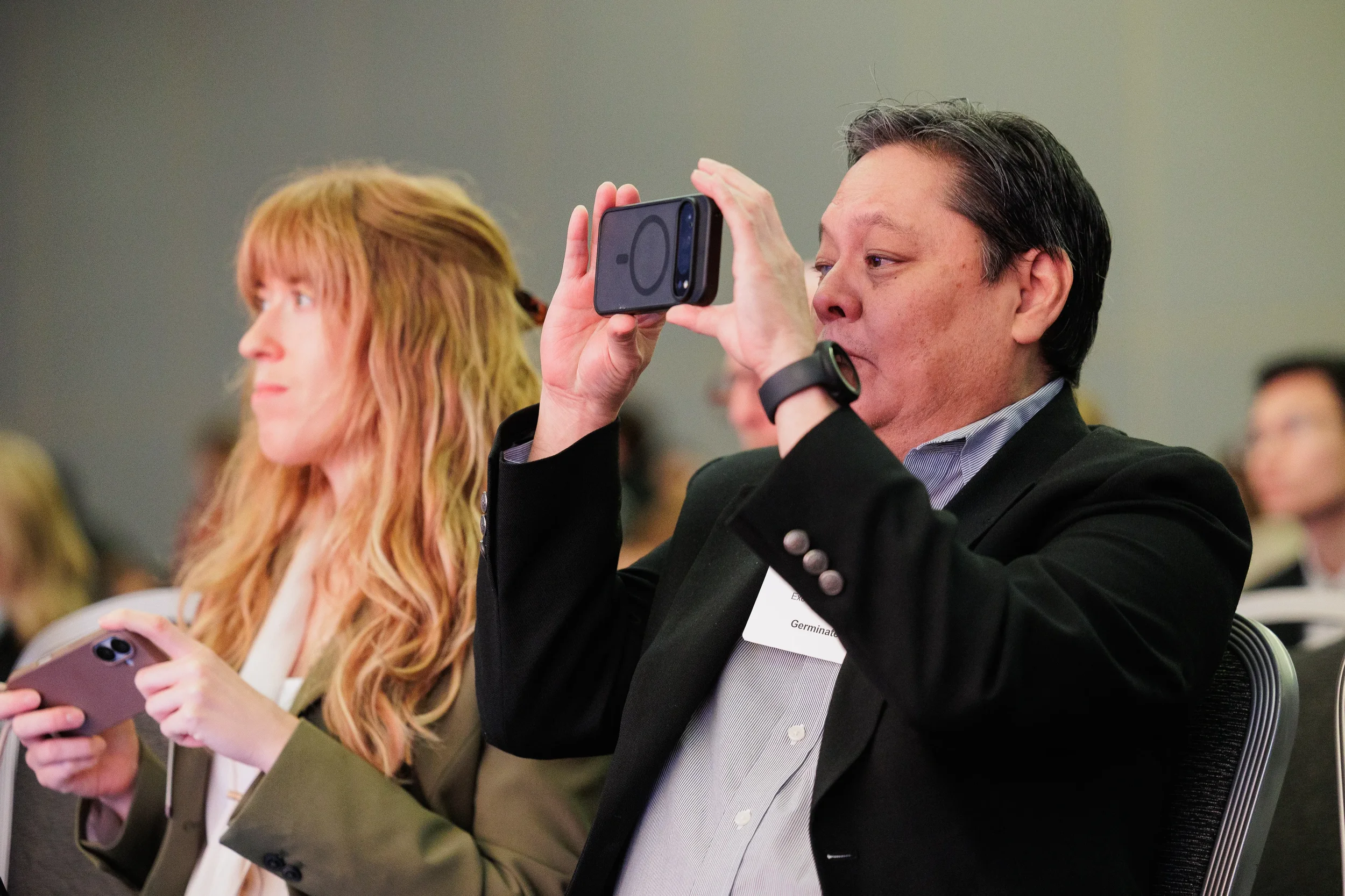 Badged attendee holds up phone to photograph presentation during session at Orlando industry conference