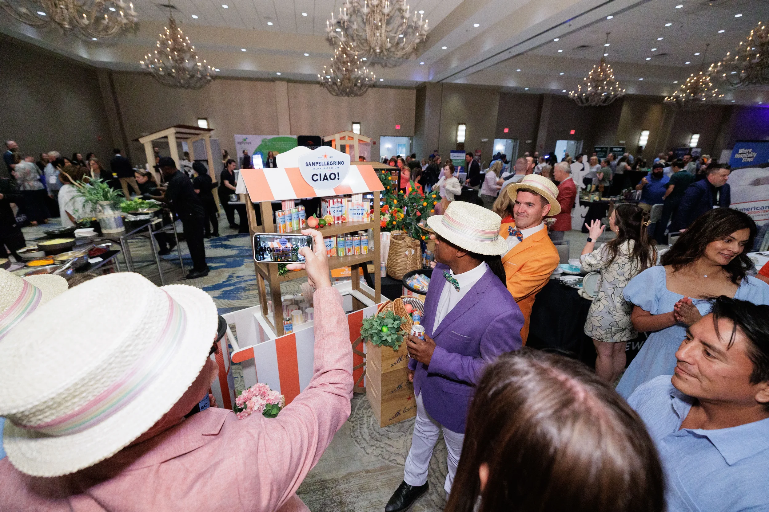 Attendees in straw hats photograph themed expo booth display in packed Orlando corporate conference ballroom