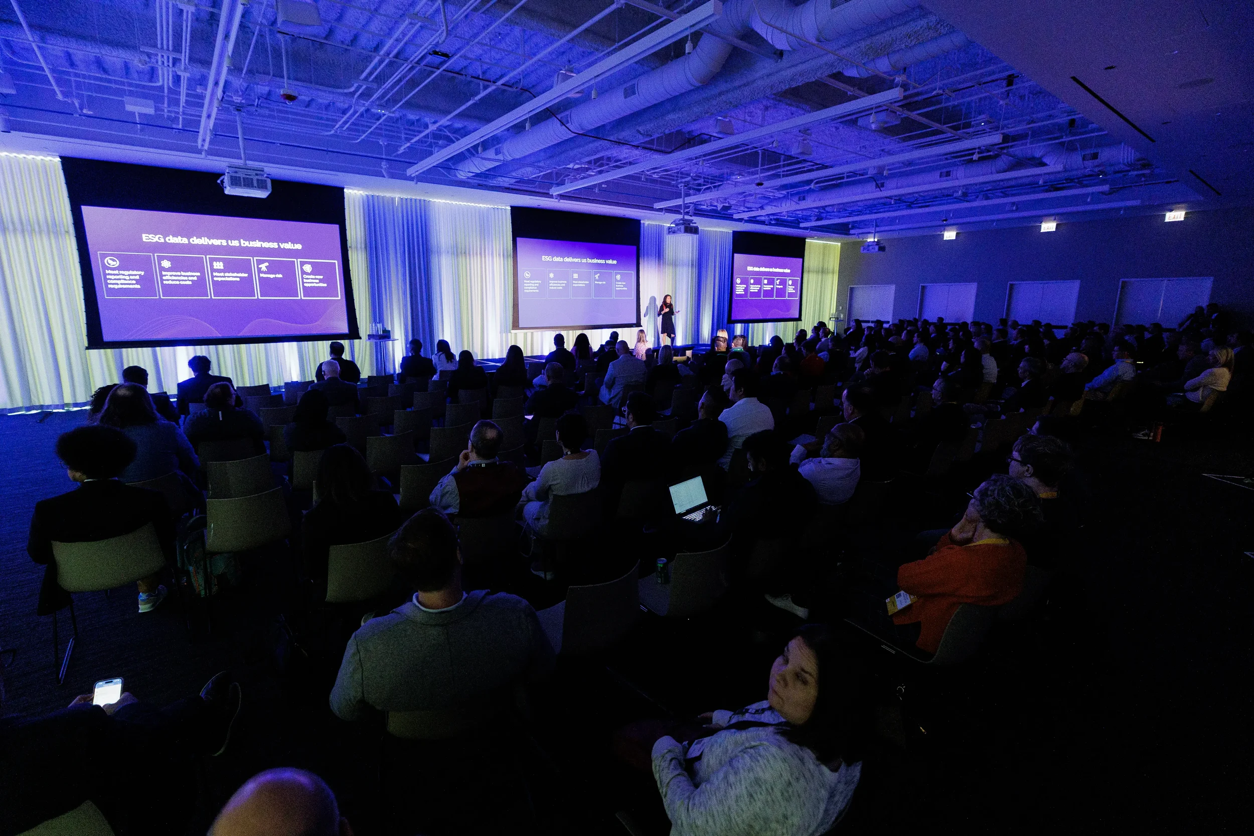 Wide view of audience watching session across three screens in purple-lit room at Chicago conference