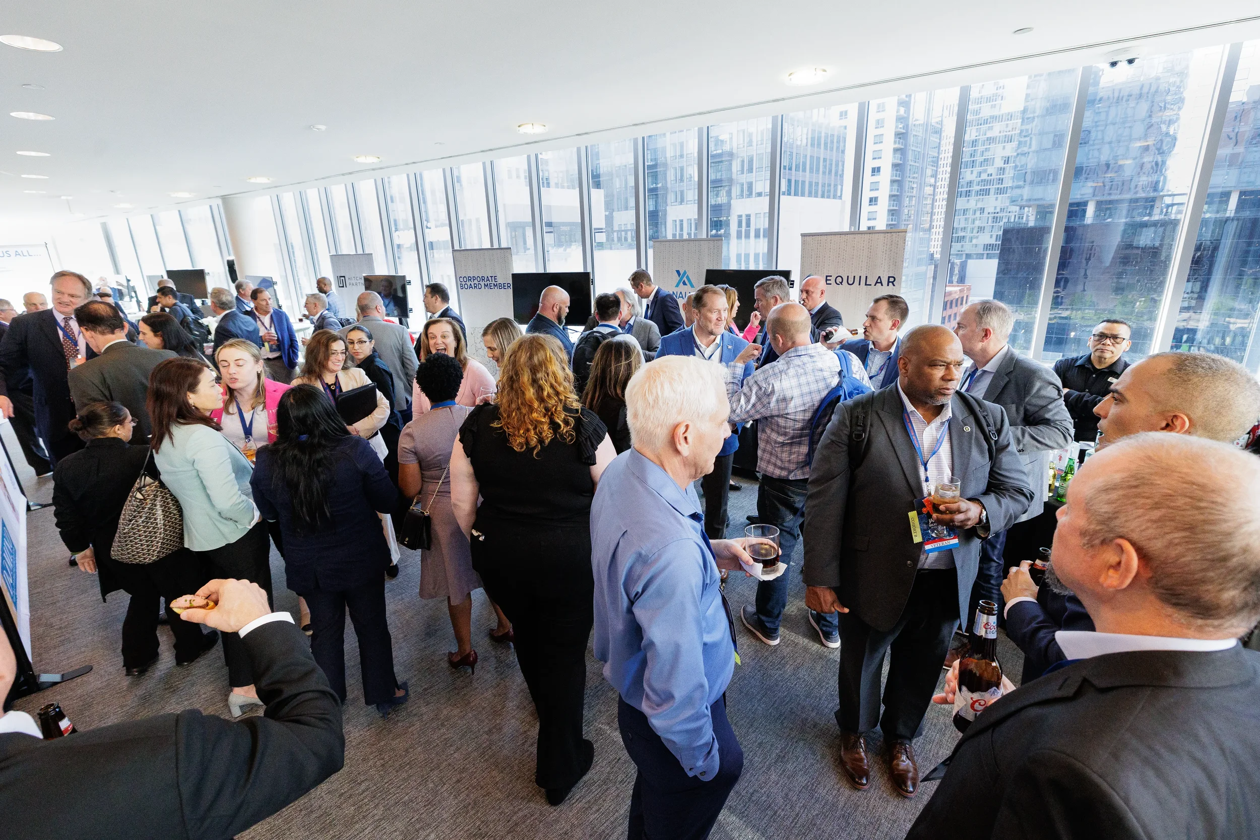 Large crowd of attendees network during reception near sponsor booths with city views at Orlando corporate event