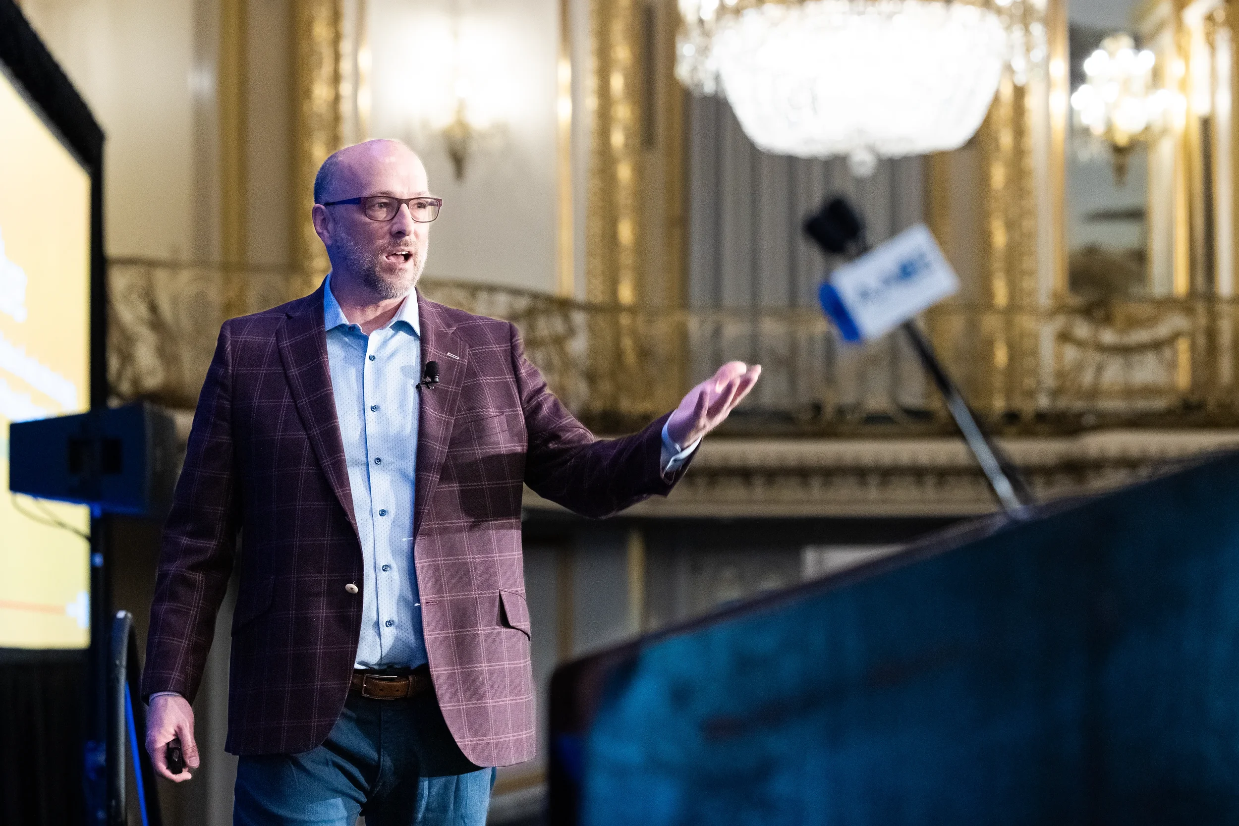 Speaker gestures while presenting to audience in ornate ballroom at Orlando industry conference