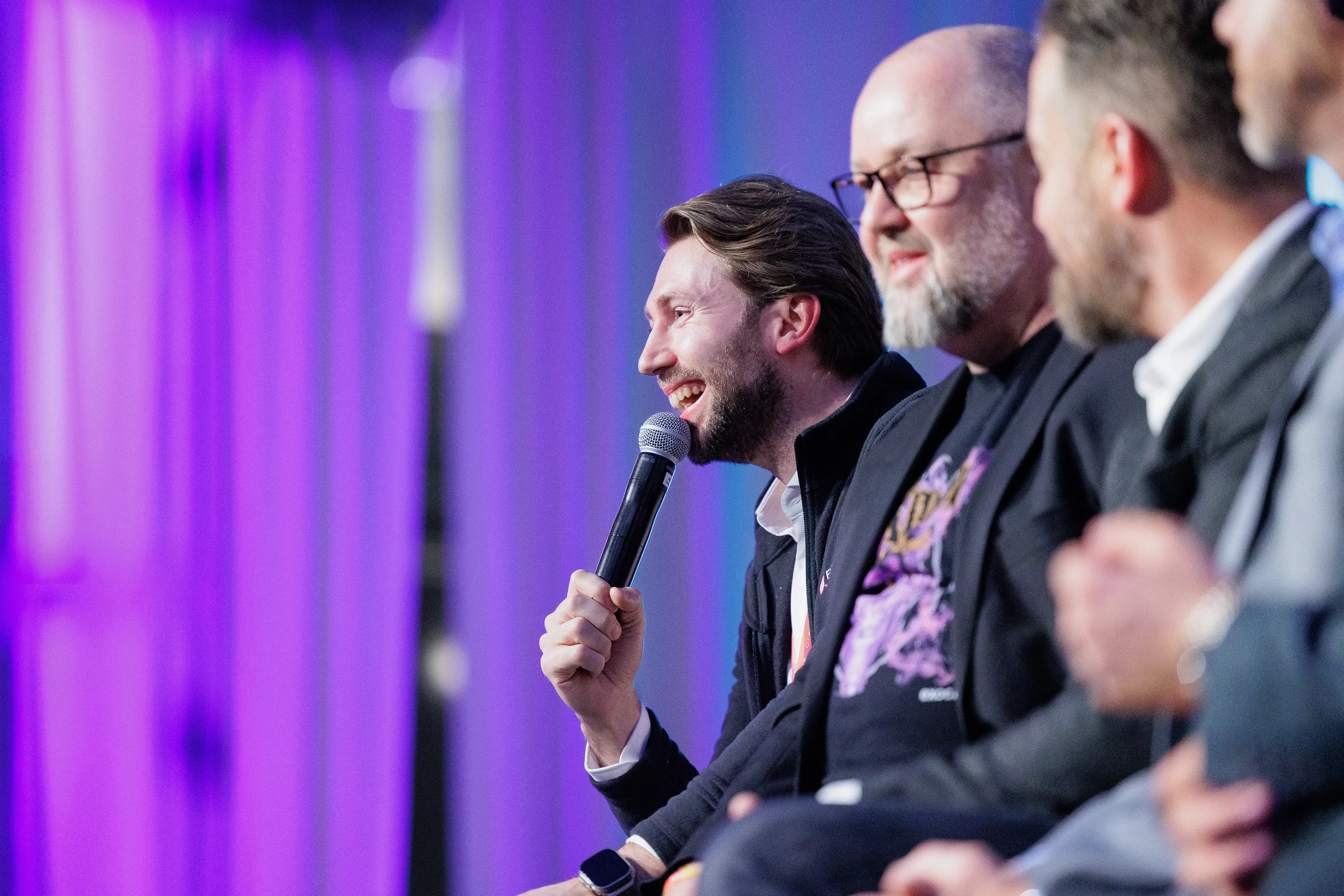 Smiling panelist speaks into microphone during panel discussion with purple lighting at Chicago corporate event