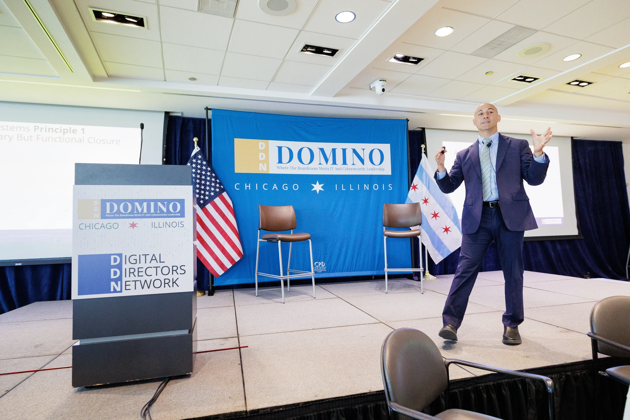 Energetic speaker gestures on branded stage beside podium and Chicago flag at Orlando corporate conference