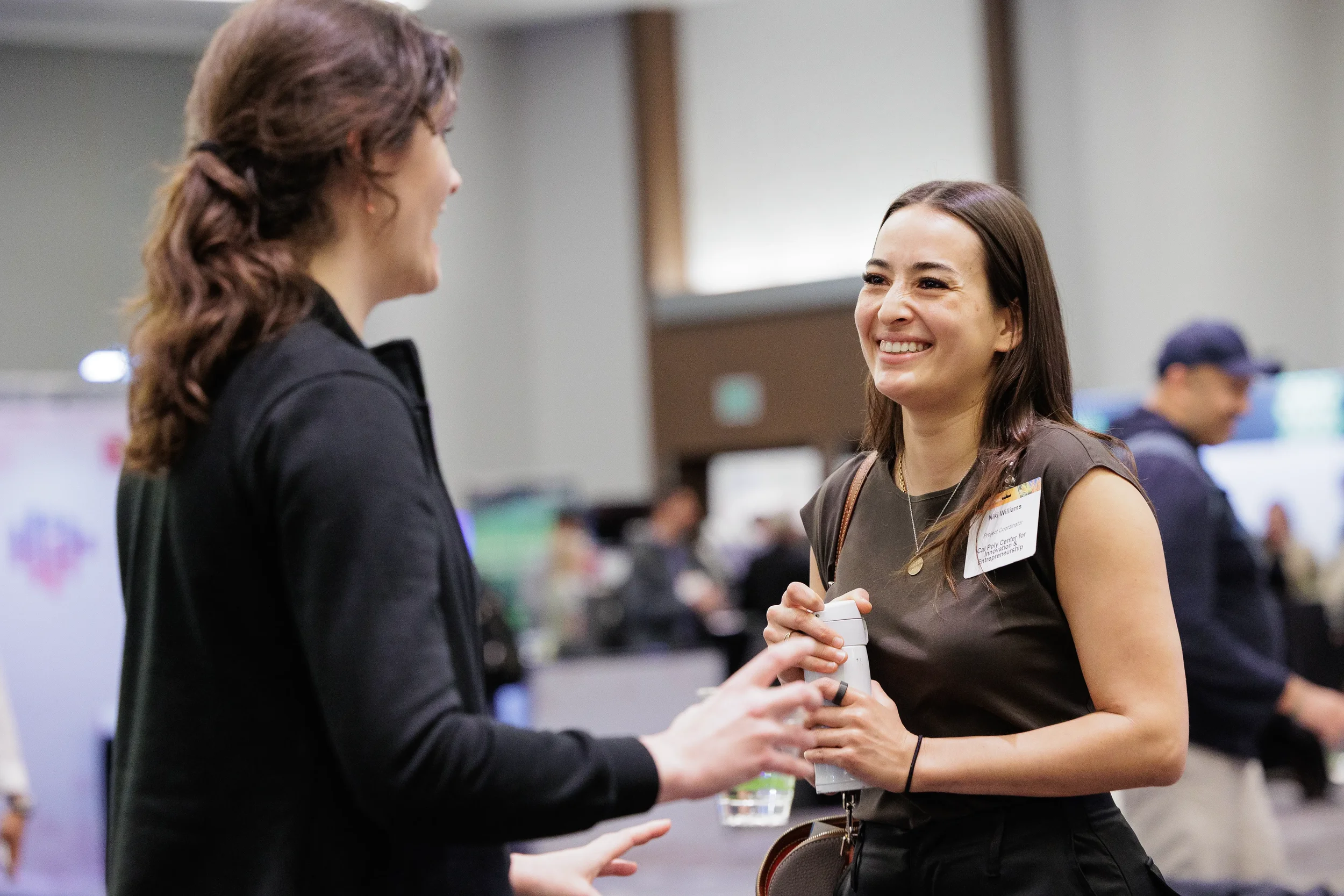 Two attendees with name badges laugh together while networking on expo floor at Orlando industry conference