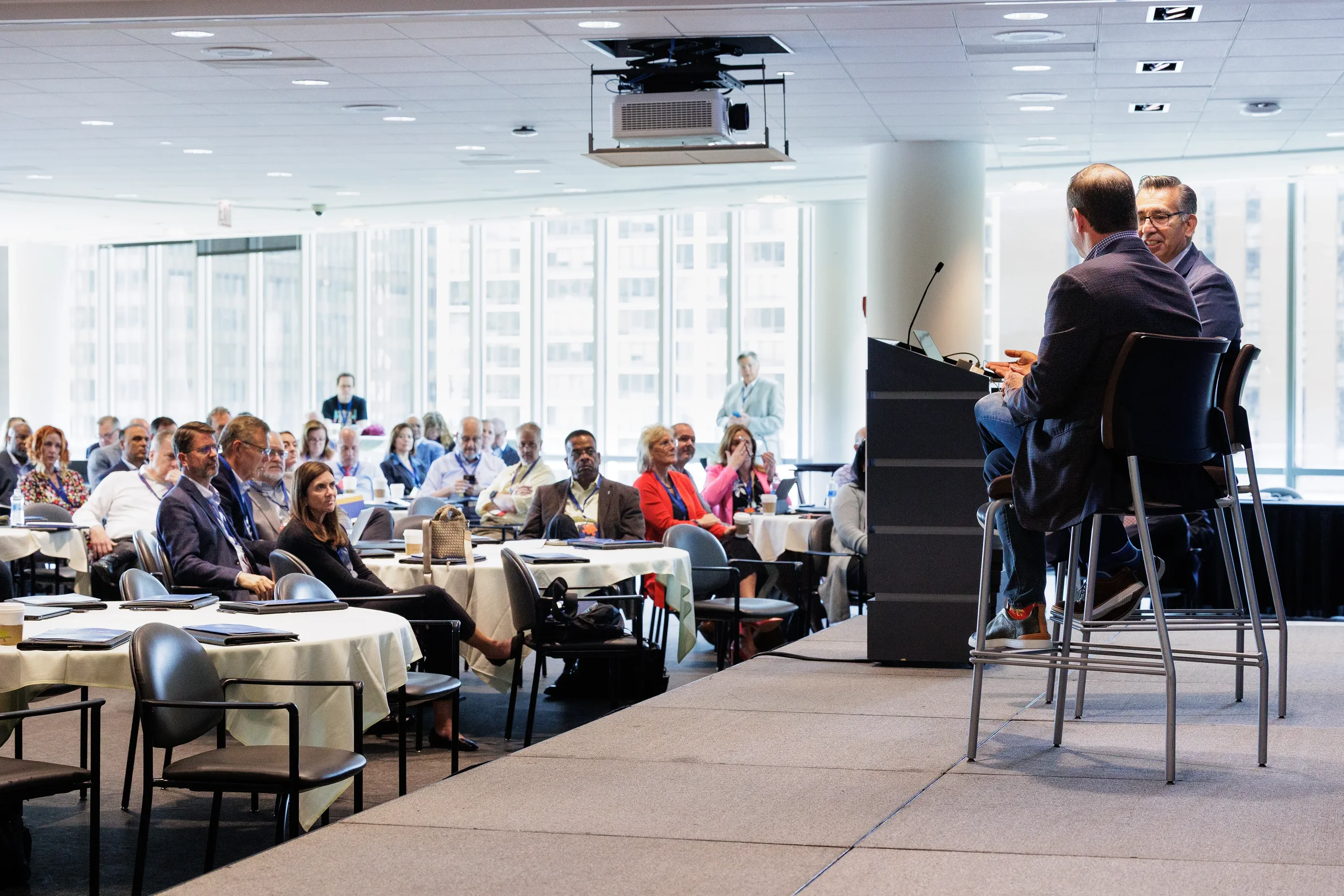 Two speakers seated on stools for fireside chat before full room of attendees at Orlando corporate conference