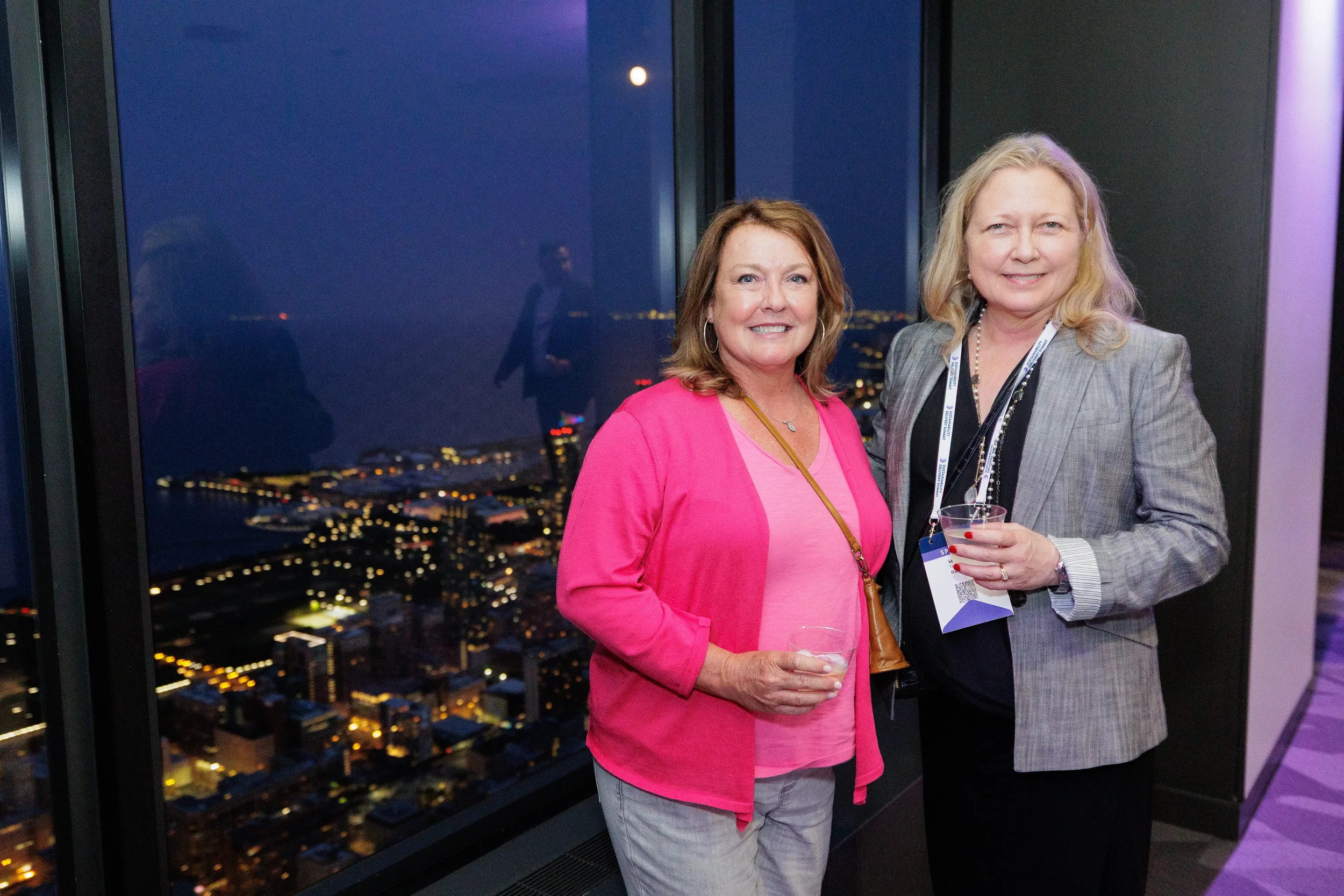 Two attendees smile together with night skyline view during Orlando corporate event reception