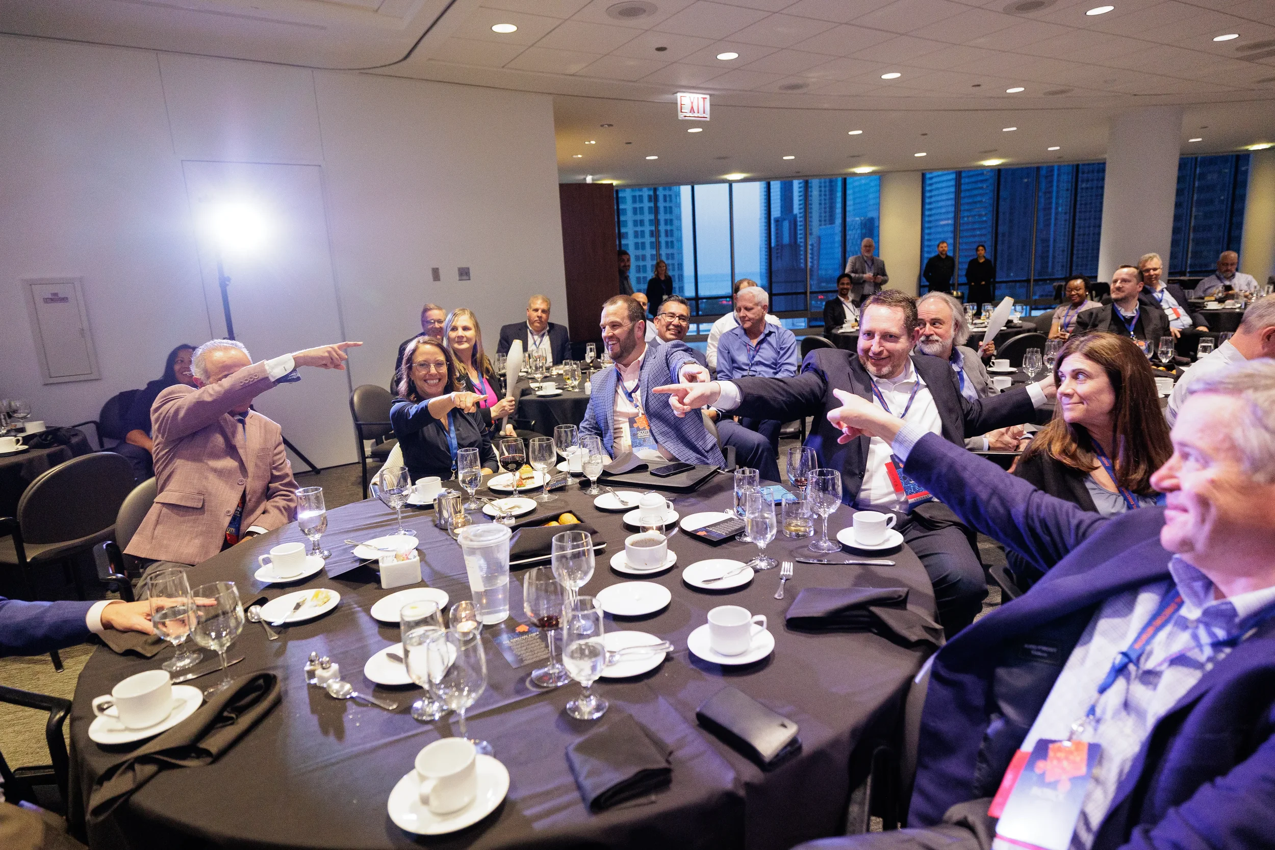 Attendees laugh and point at round dinner table during Orlando corporate conference evening event with city views