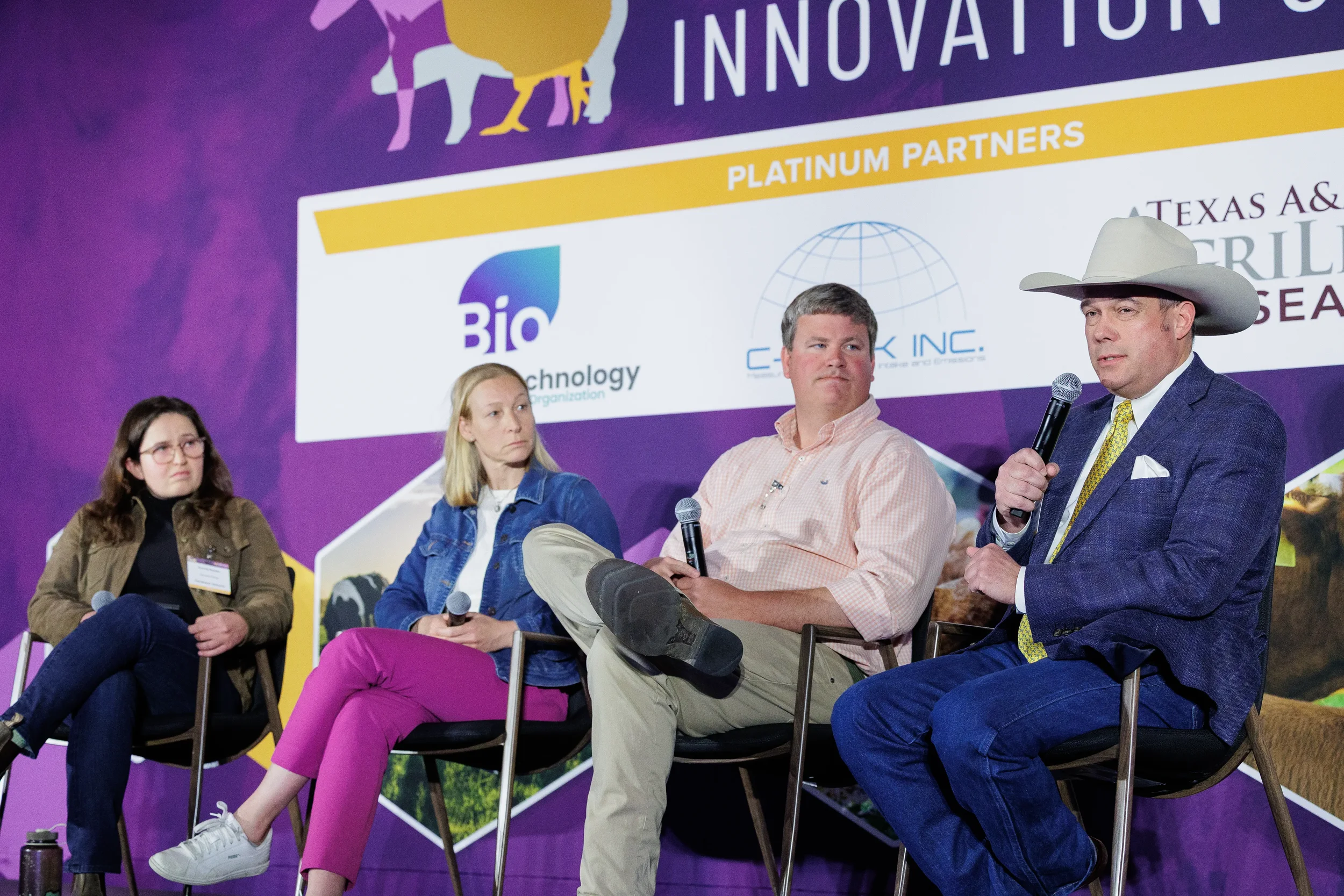 Four panelists including speaker in cowboy hat discuss on branded stage at Chicago summit