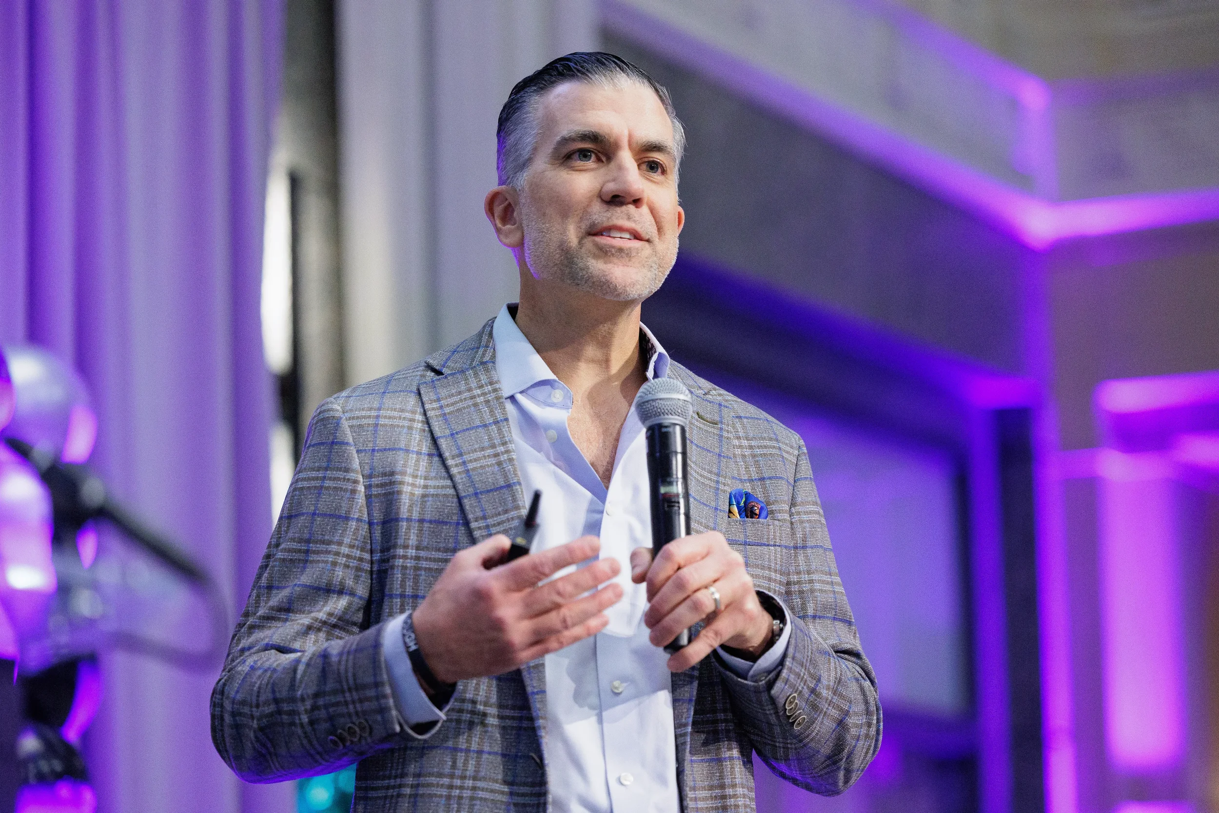Keynote speaker holds microphone and gestures while presenting on stage at Orlando corporate event