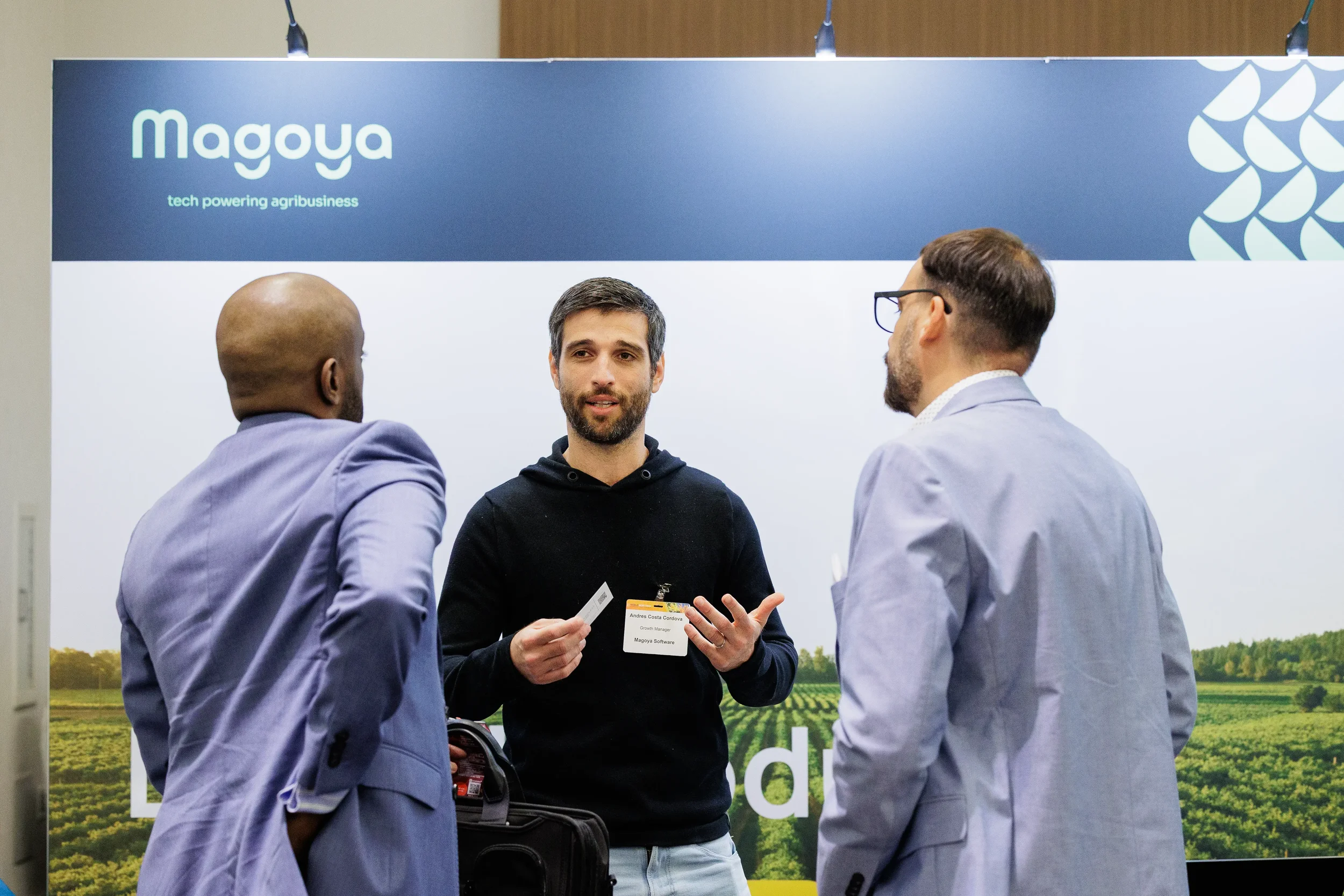 Badged exhibitor holds business card while speaking with two attendees at Orlando corporate conference trade show booth