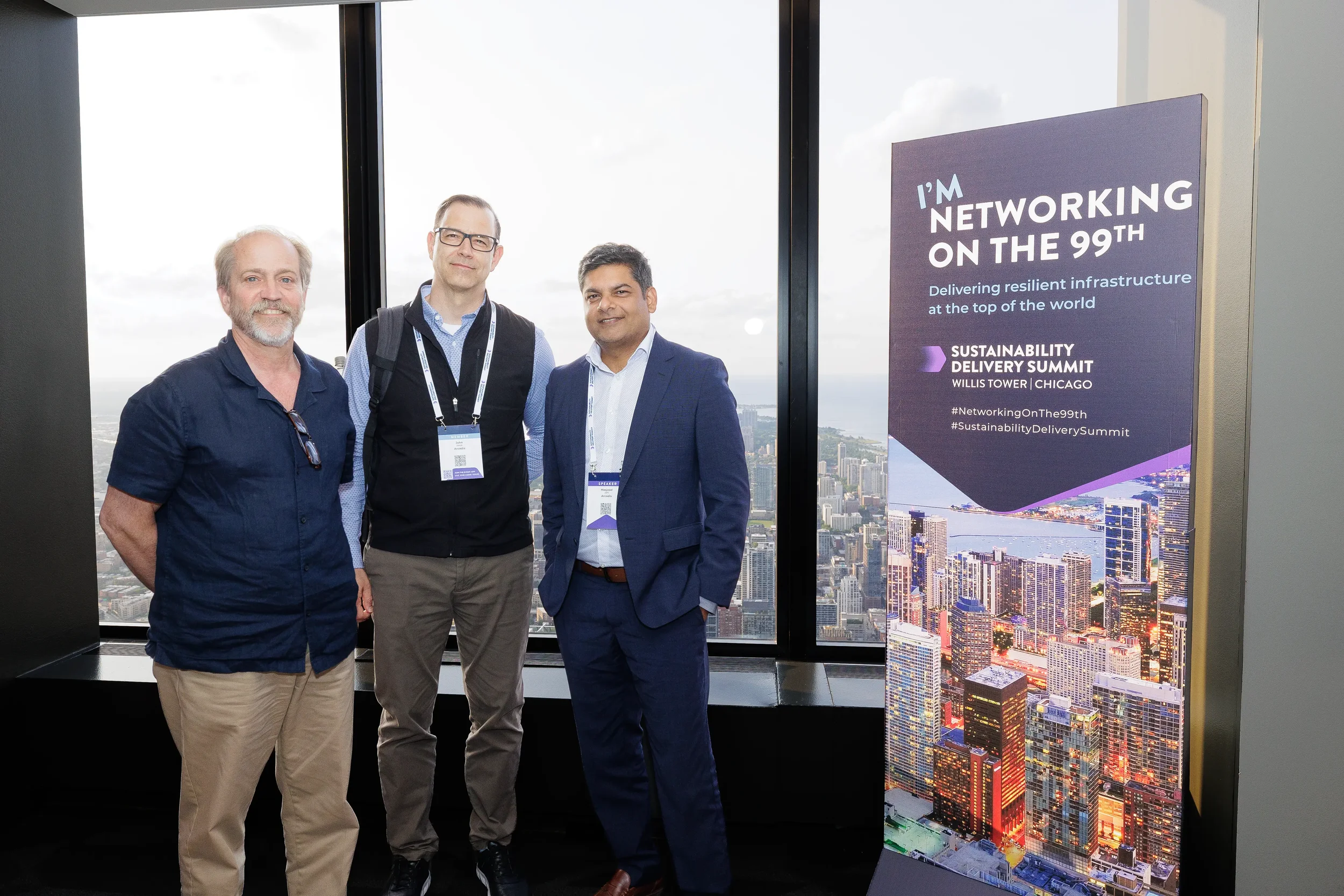 Three attendees pose for group photo near networking sign with skyline view at Orlando conference