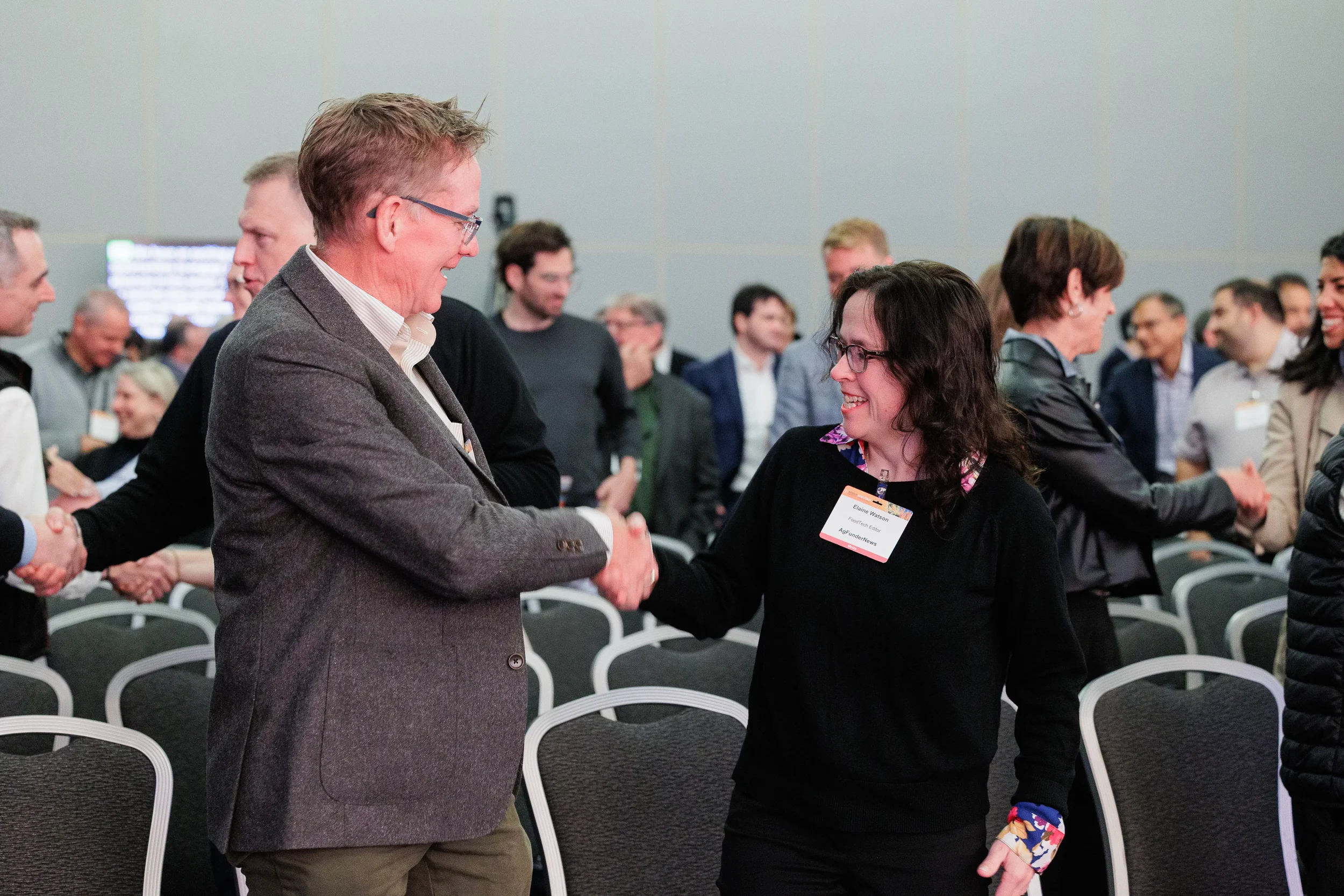 Two attendees shake hands and smile during networking activity in session room at Orlando industry conference