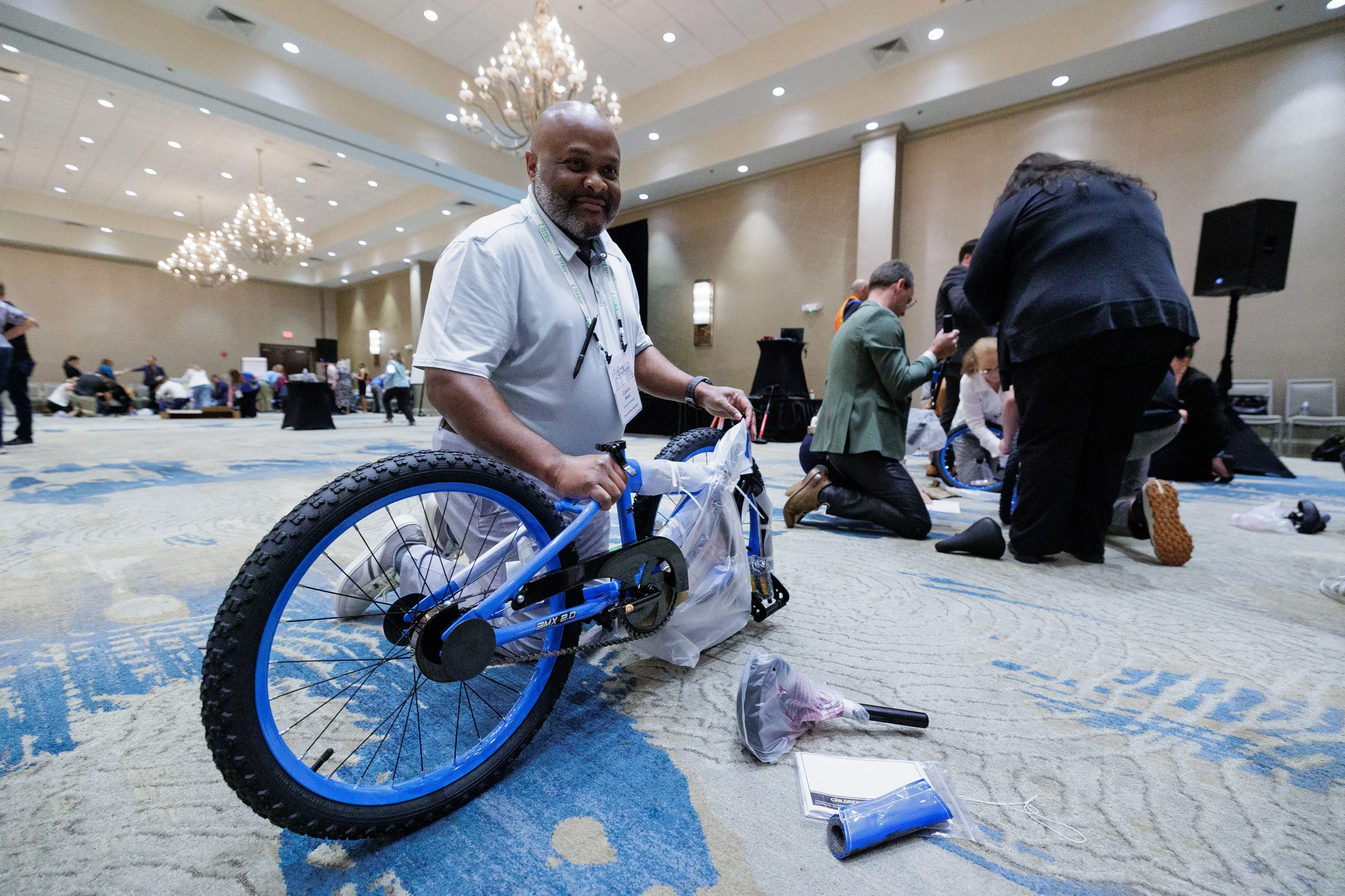 Attendee with lanyard kneels on ballroom floor assembling bicycle during Orlando corporate team activity