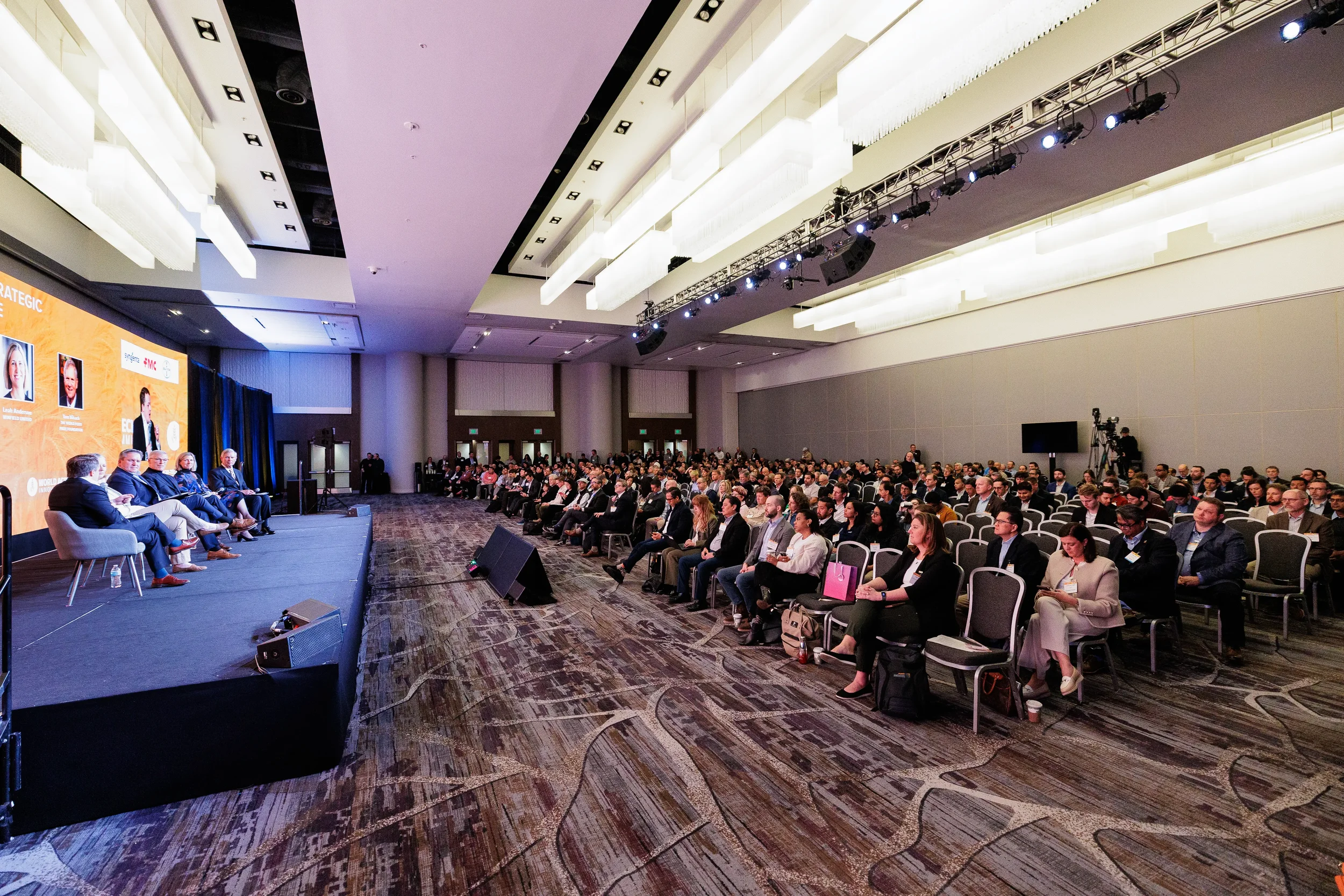 Large ballroom audience watches panel of speakers on branded stage at Orlando corporate industry conference