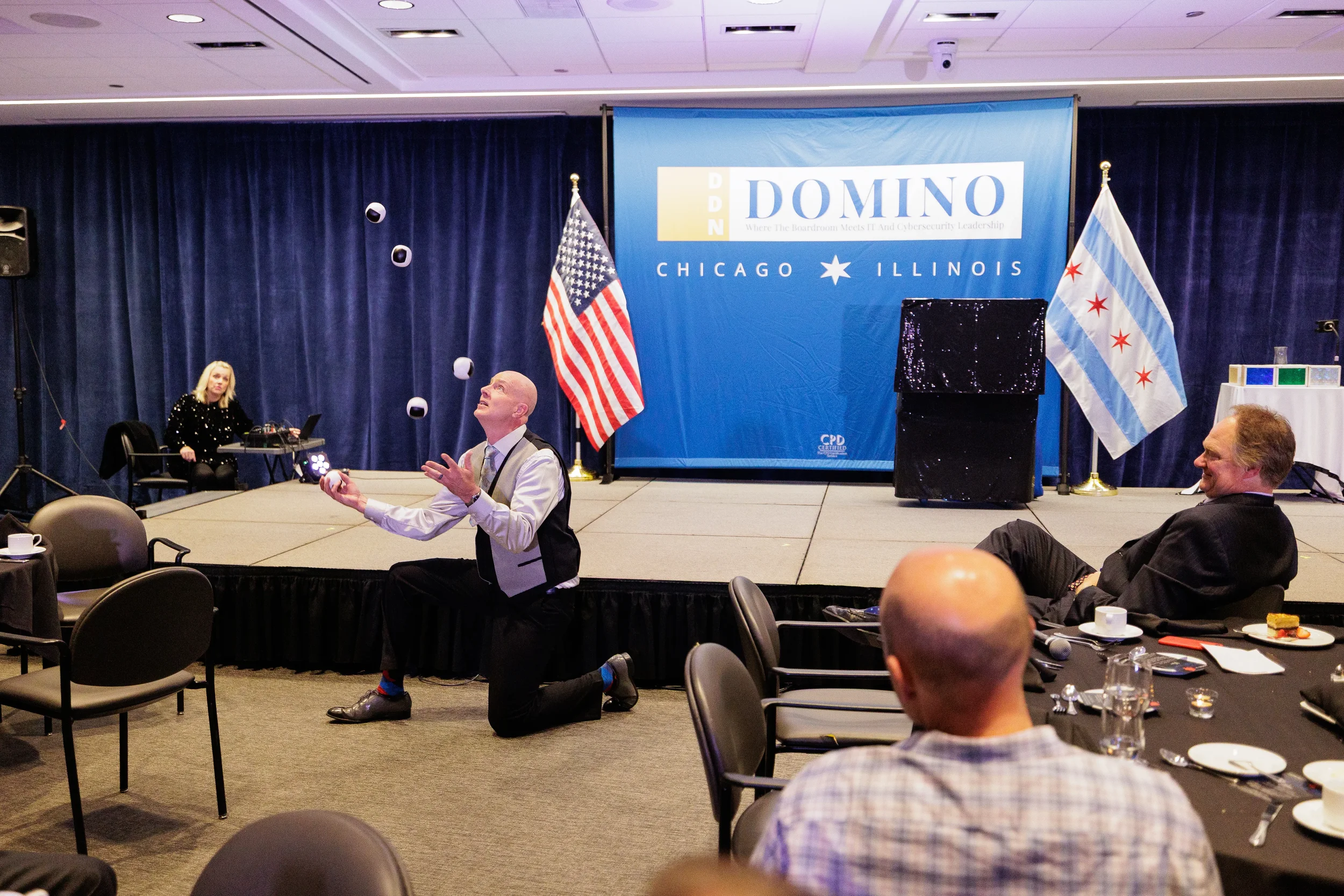 Entertainer kneels while juggling balls in front of branded stage backdrop with flags at Chicago corporate event