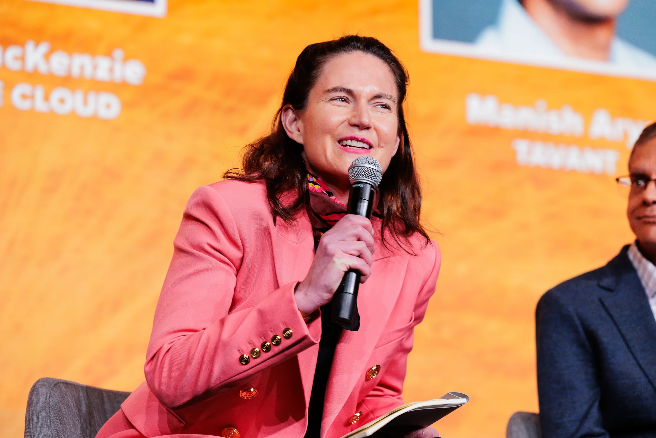Speaker in pink blazer smiles while presenting with microphone on stage at Chicago industry summit