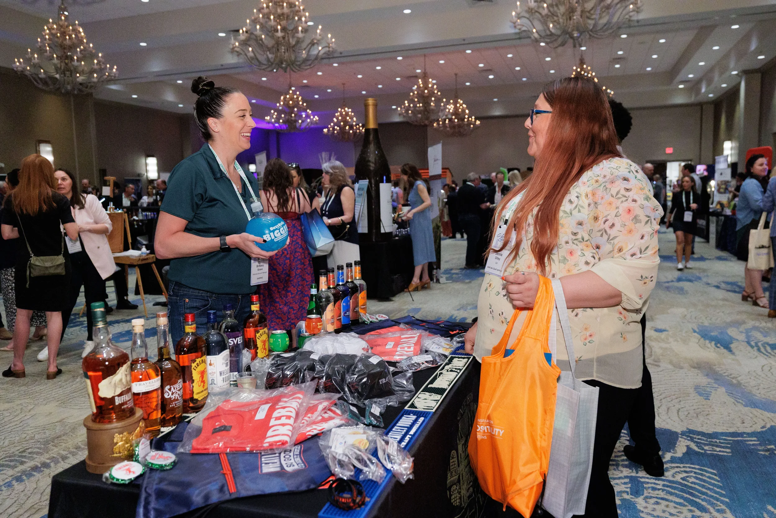 Booth staff chats with attendee beside table of giveaways and bottles at Orlando industry conference