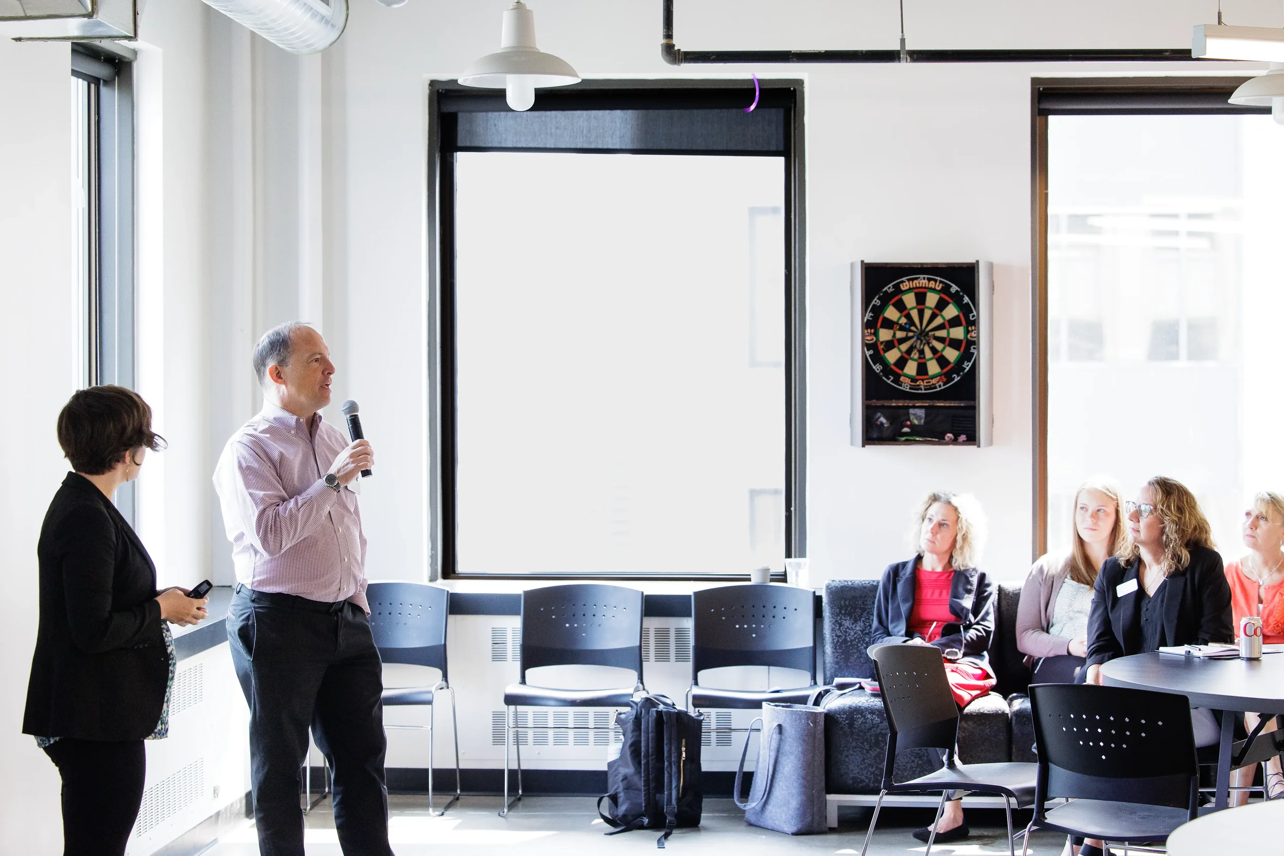 Male presenter with microphone stands beside colleague addressing seated attendees at Orlando conference