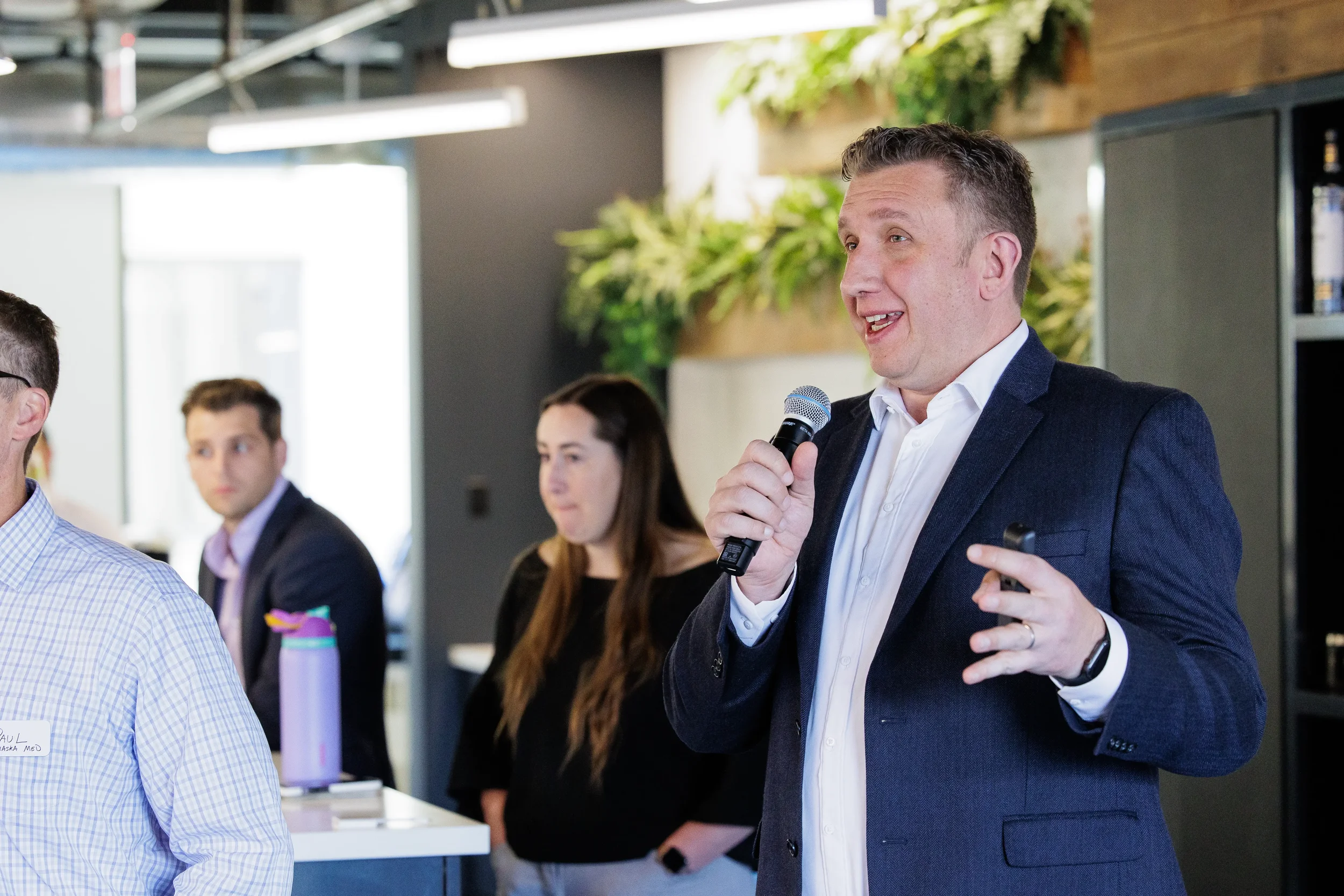Male speaker addresses a group with microphone in front of greenery wall at Chicago industry conference