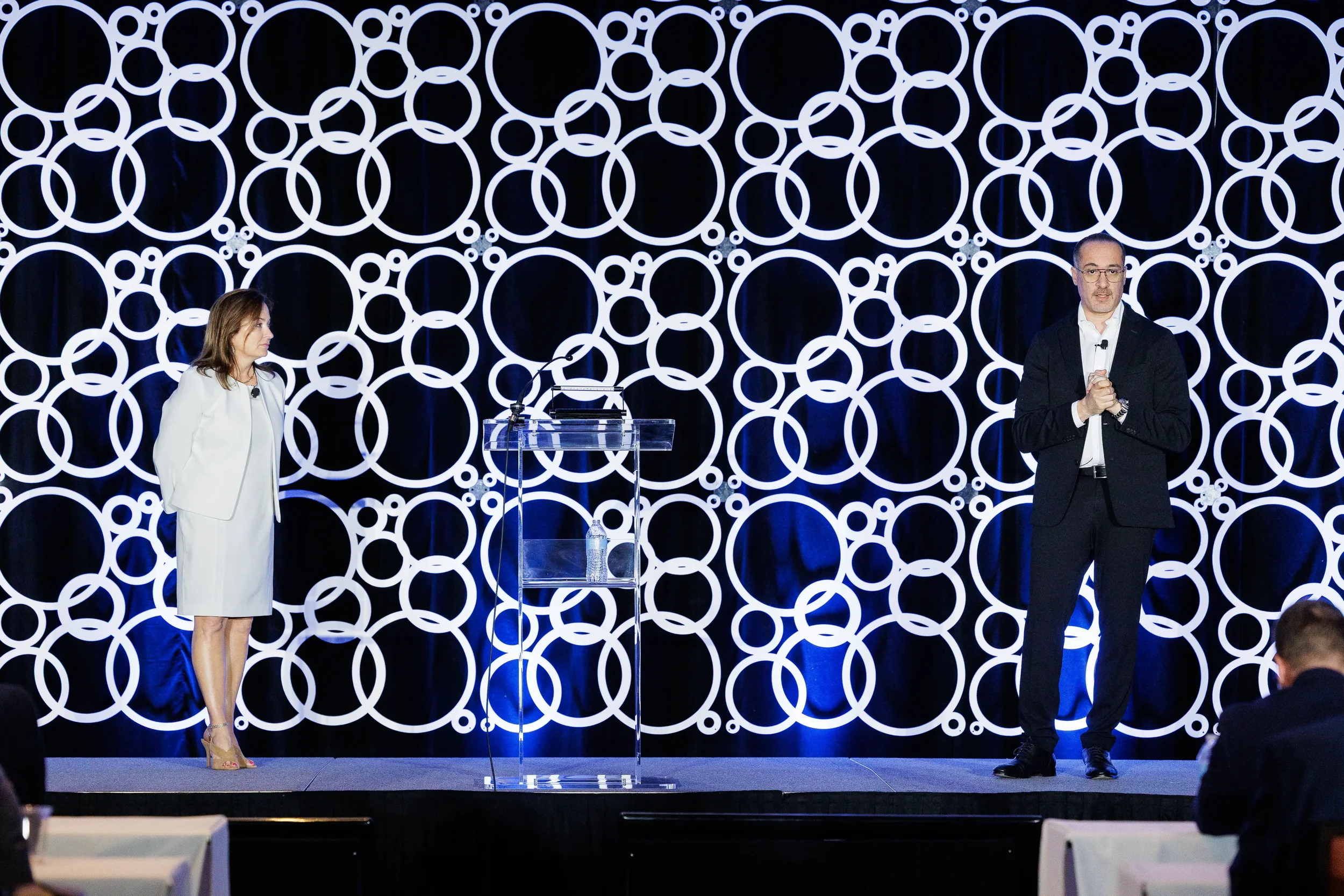 Two speakers present on stage with illuminated circular backdrop at Chicago industry conference