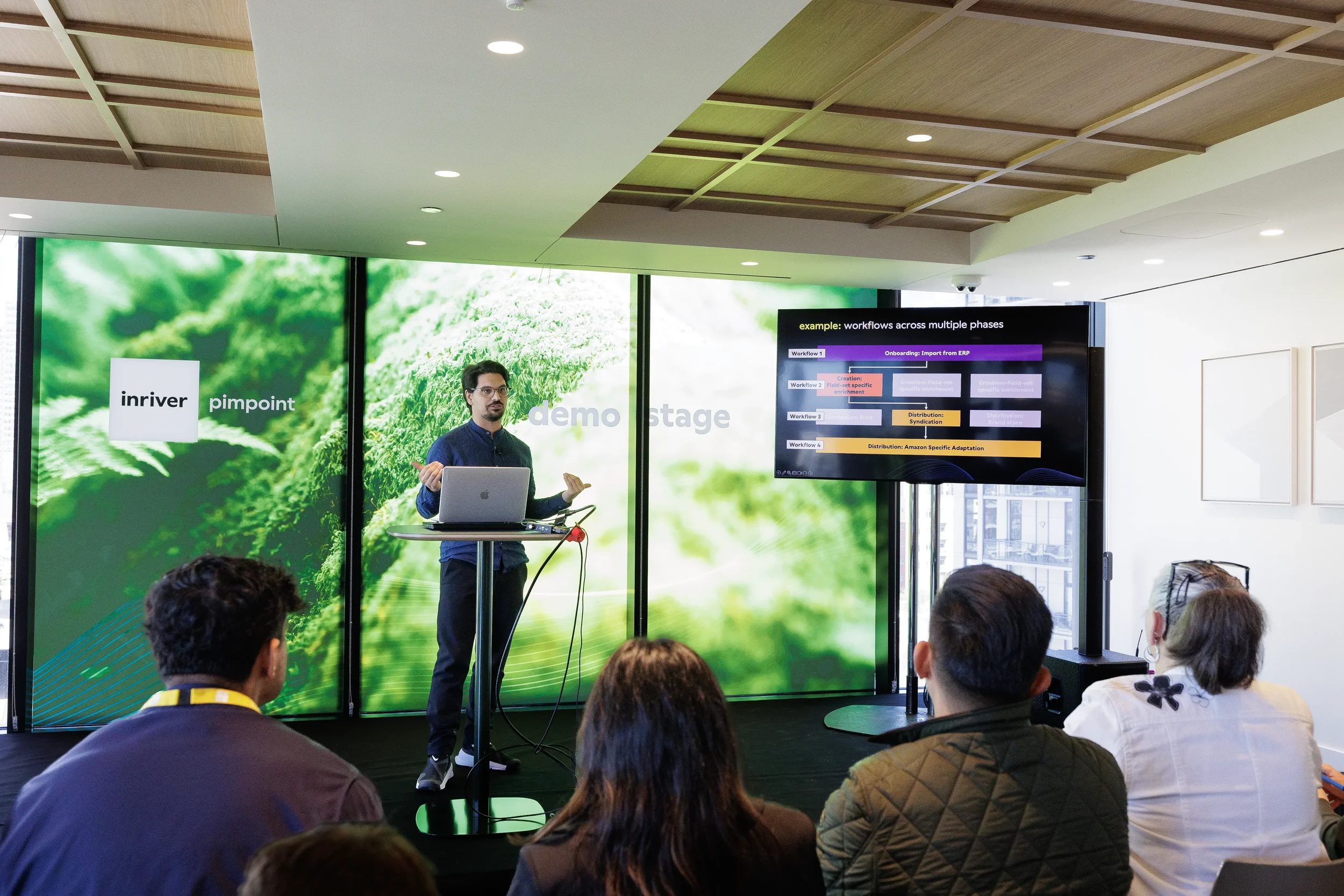 Presenter with laptop gives demo to audience beside workflow screen at Chicago industry conference
