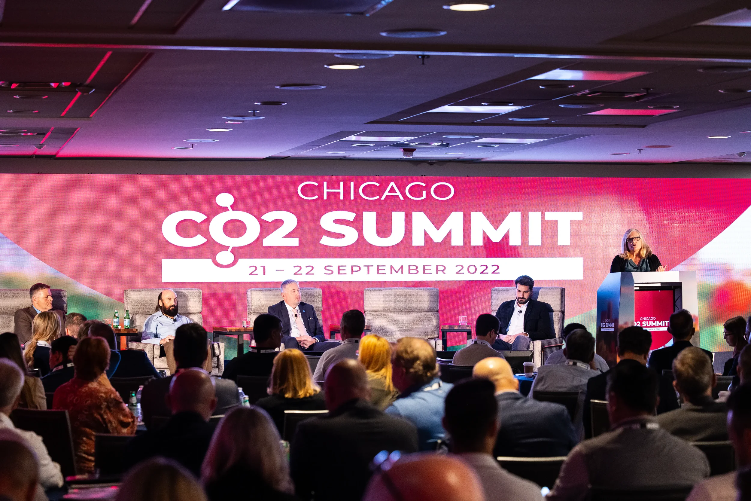 Panelists and moderator on stage before a full audience during panel discussion at Orlando conference