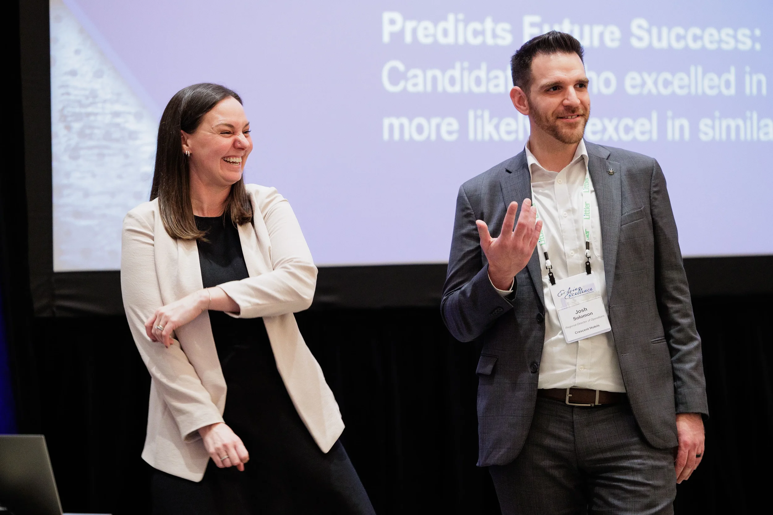 Two presenters laugh together on stage in front of projection screen at Chicago corporate conference