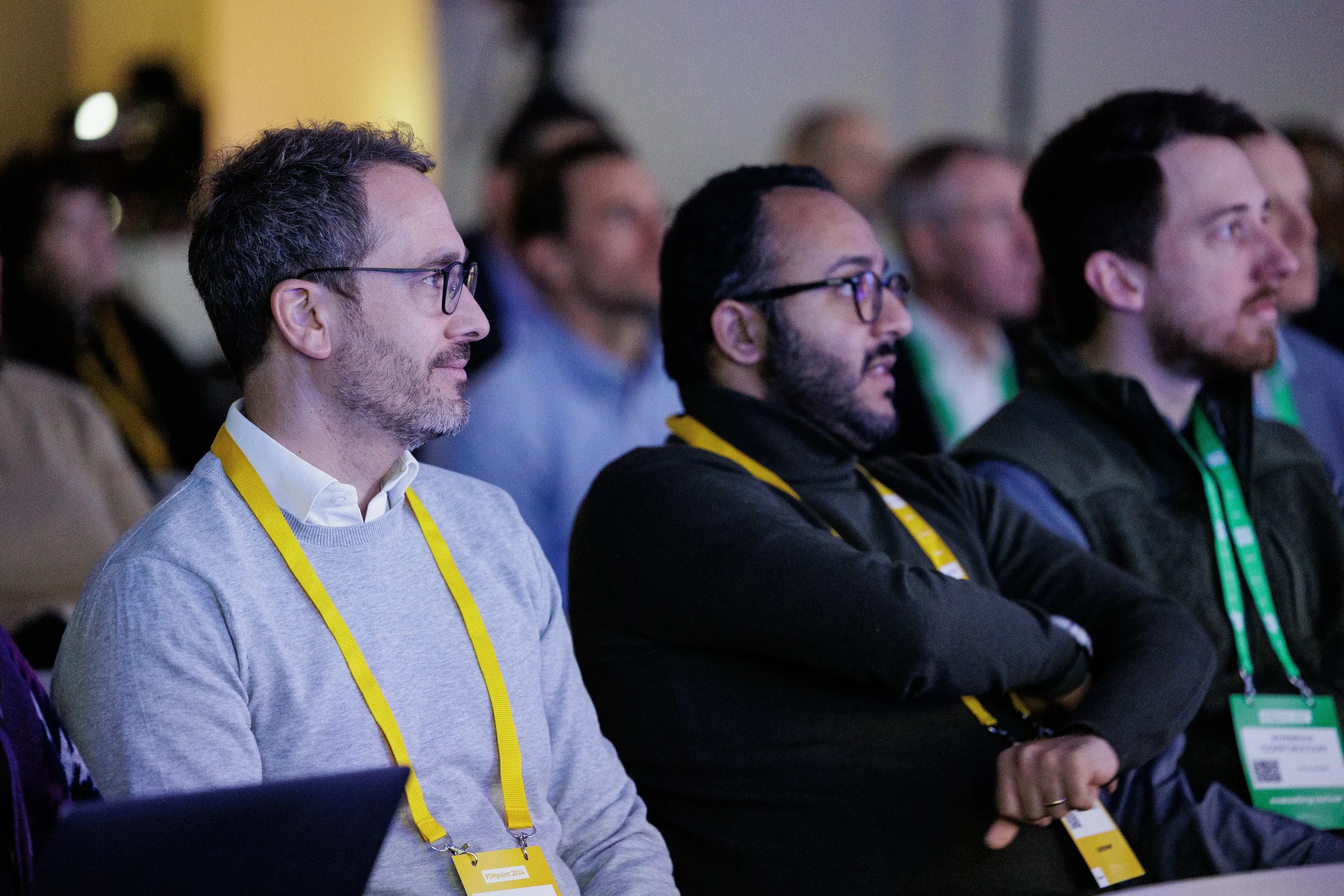 Attendees with yellow lanyards watch session intently in dim light at Orlando industry conference