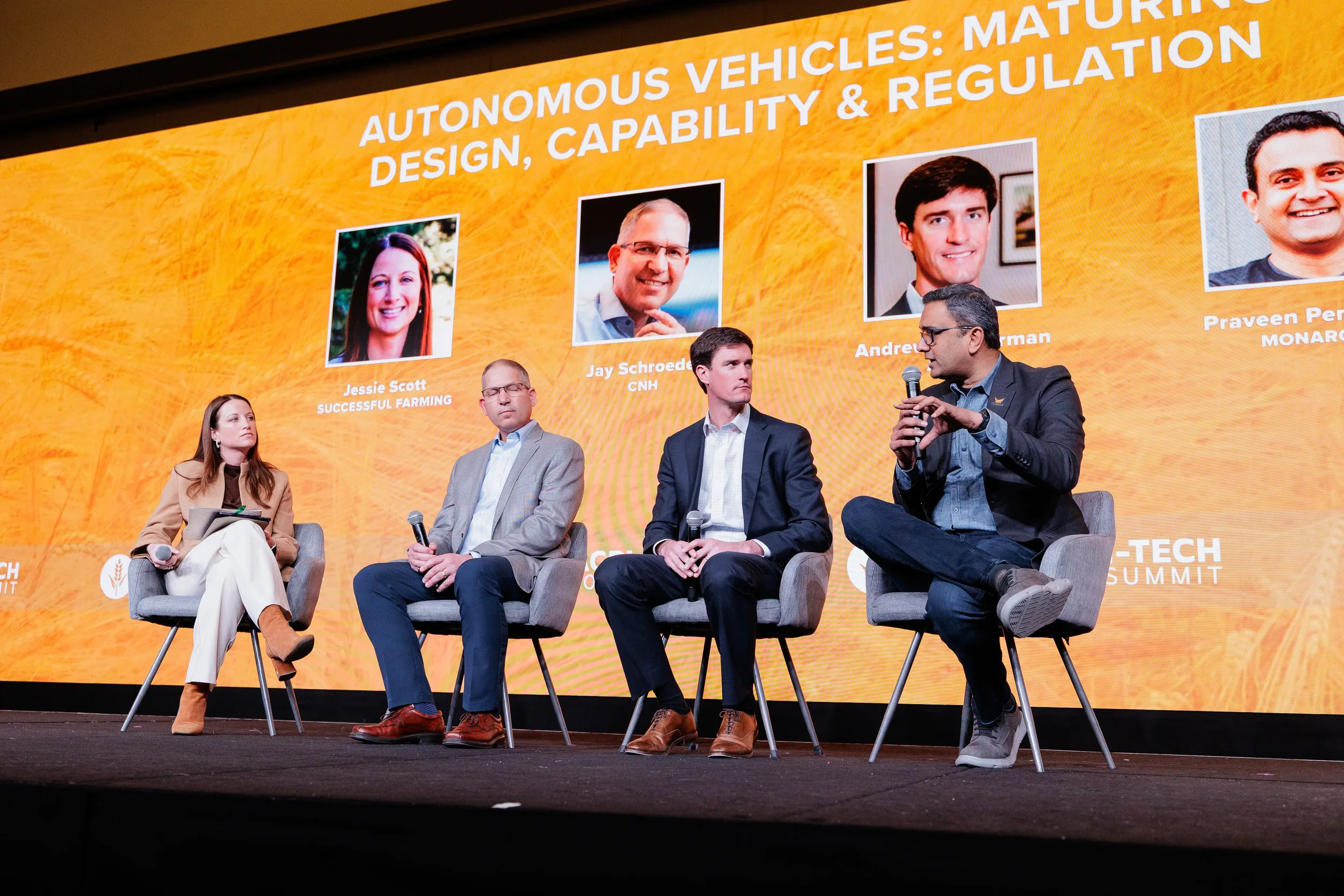 Four panelists with microphones seated on stage with orange branded backdrop at Chicago industry conference