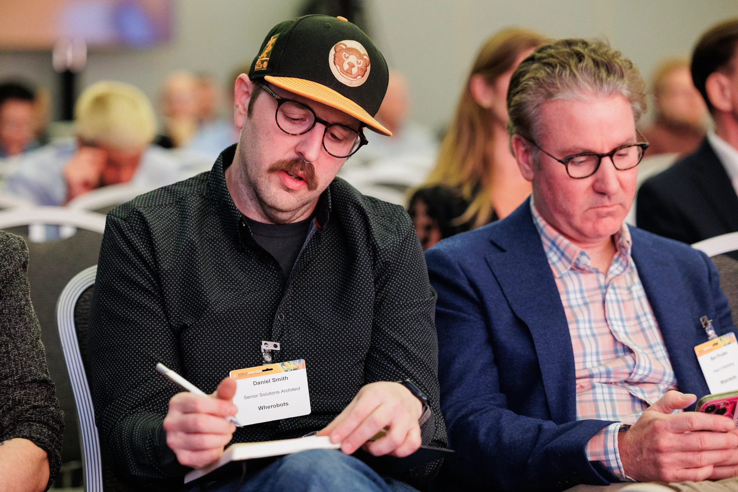 Two attendees with name badges take notes during seated session at Chicago industry conference