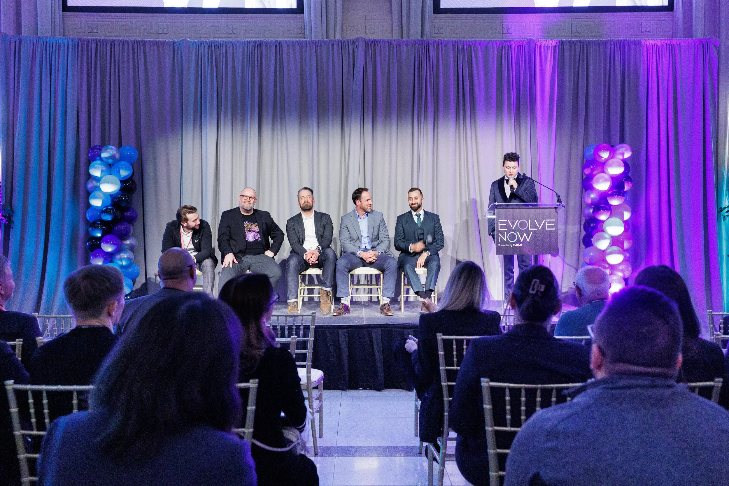 Full panel of speakers on stage with moderator at podium viewed from audience at Orlando conference