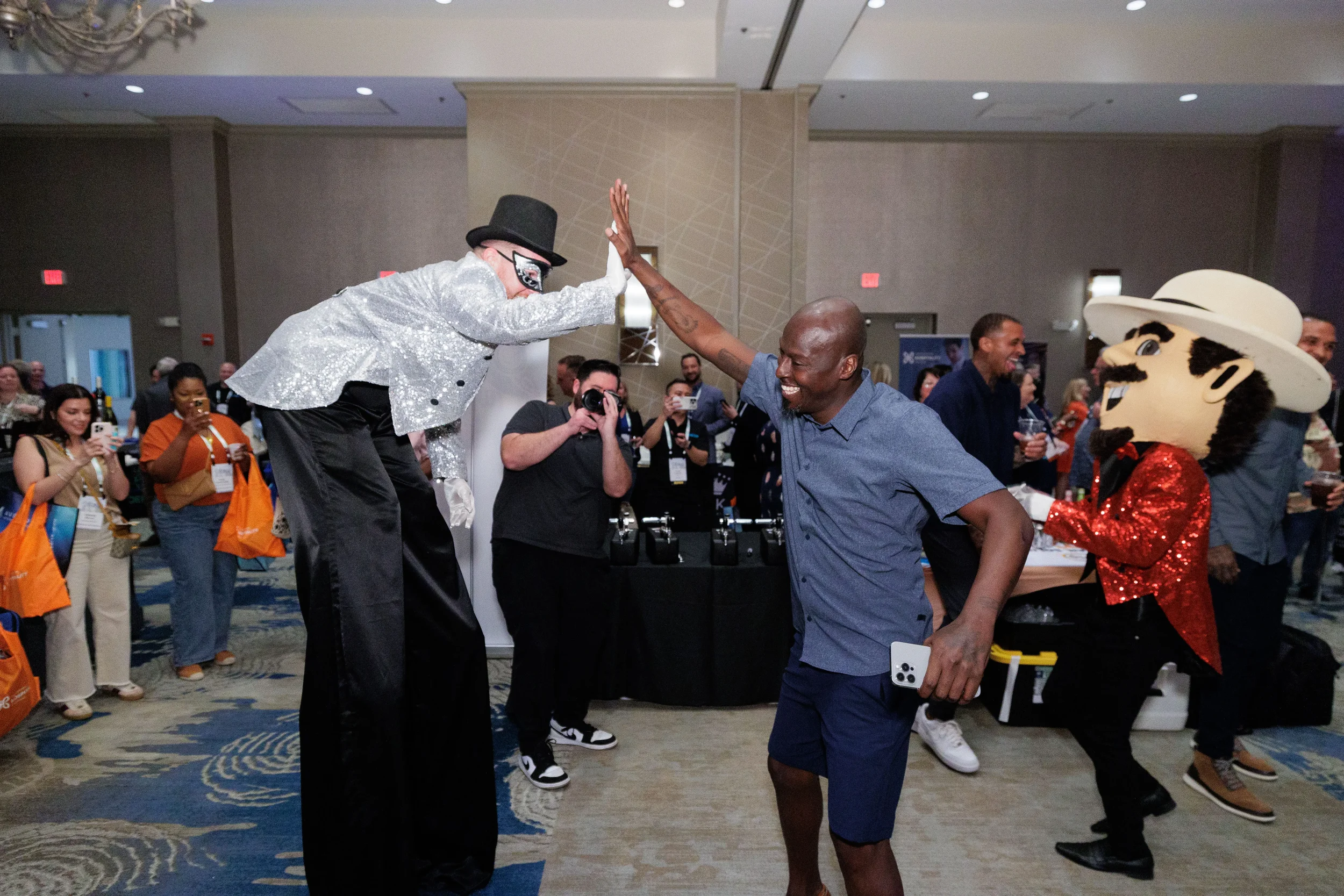 Stilt performer high-fives laughing attendee as costumed mascot looks on at Orlando corporate event