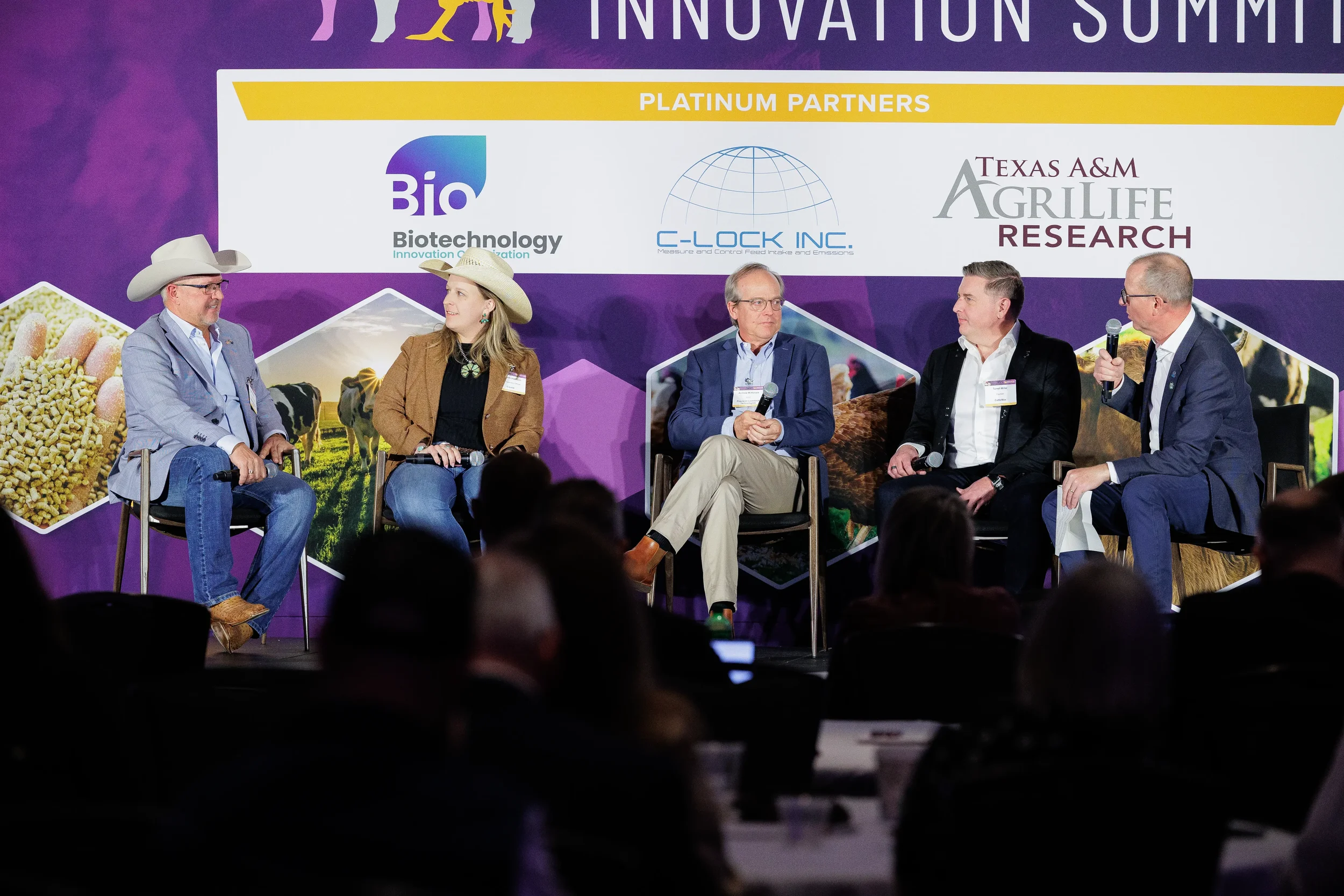 Five panelists seated on stage before audience at Chicago industry conference sponsor banner