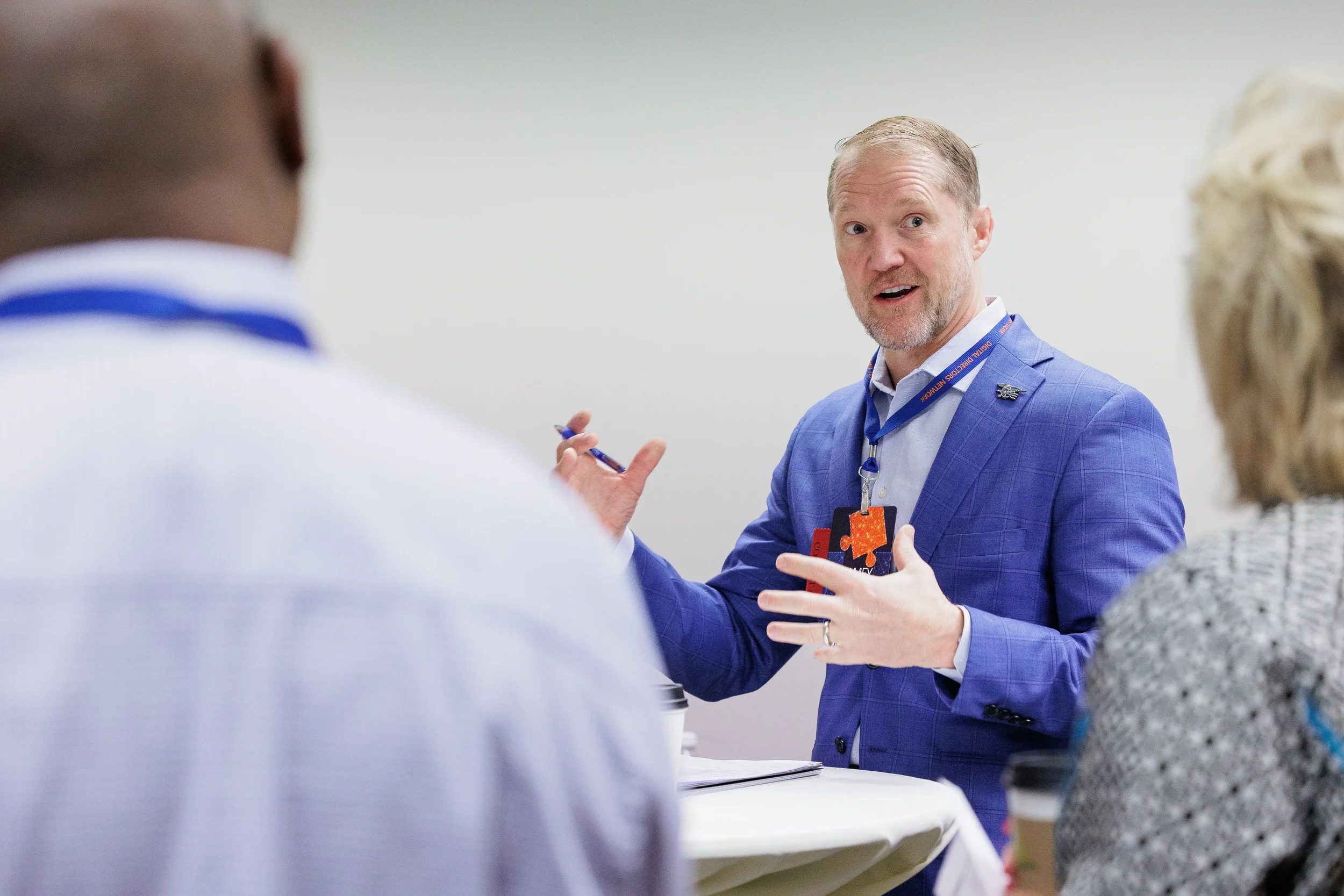 Male attendee with lanyard gestures while speaking in small group discussion at Chicago industry conference