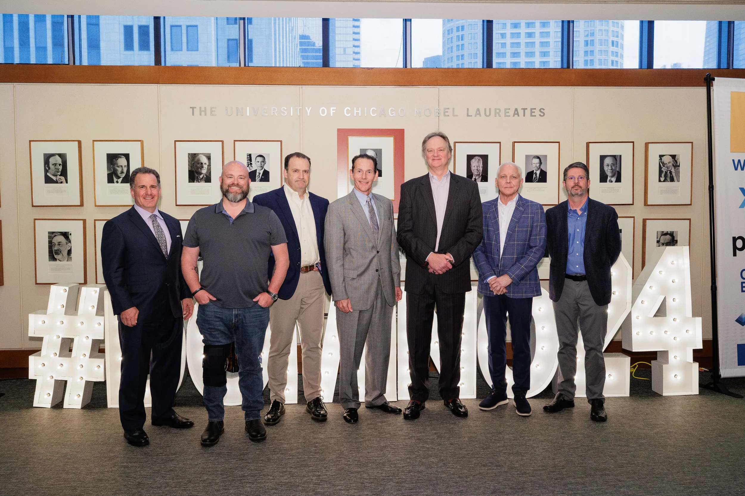 Seven male attendees with lanyards pose for group photo in front of large marquee letters at Orlando corporate event