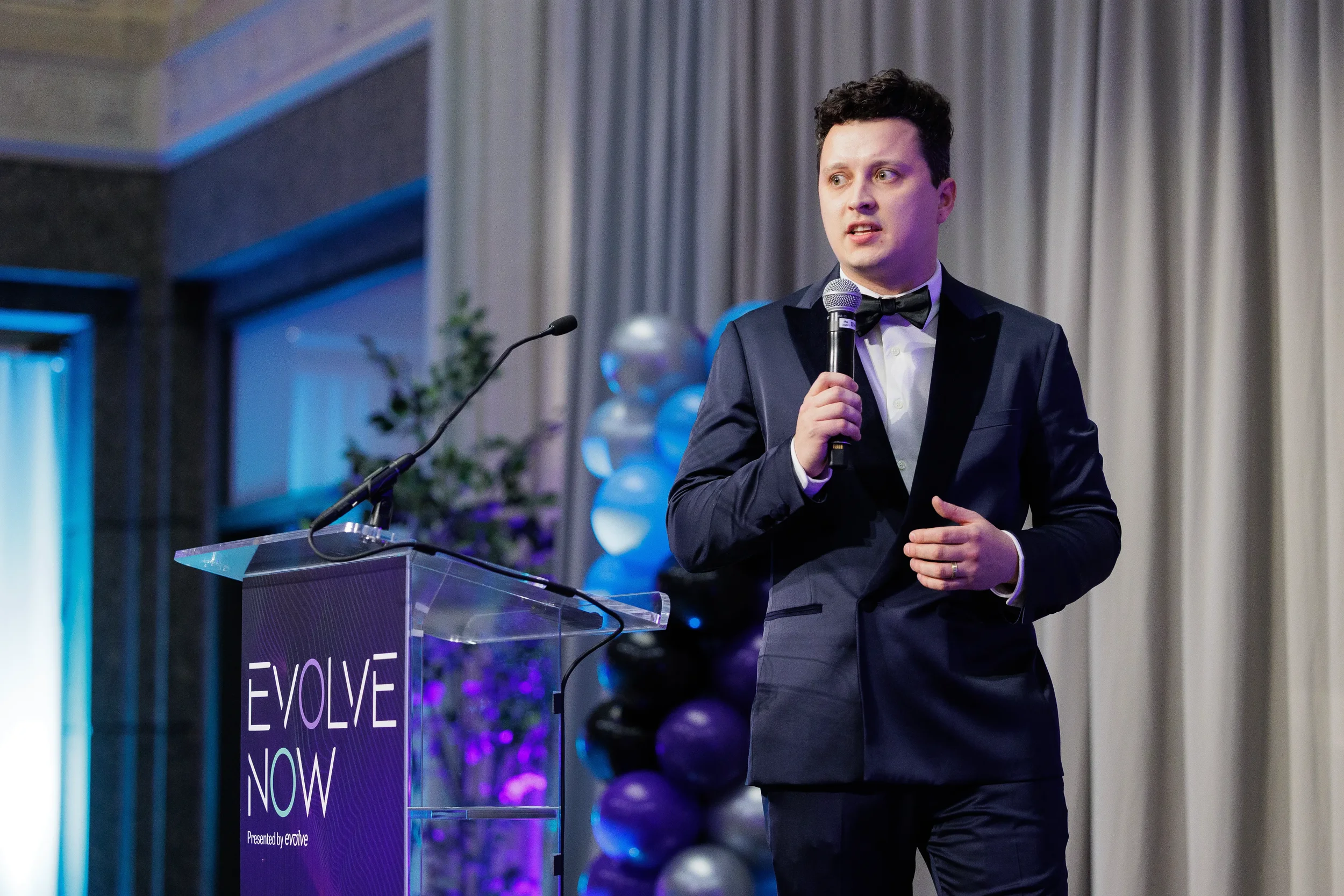 Speaker in tuxedo holds microphone at branded podium during Chicago industry corporate event