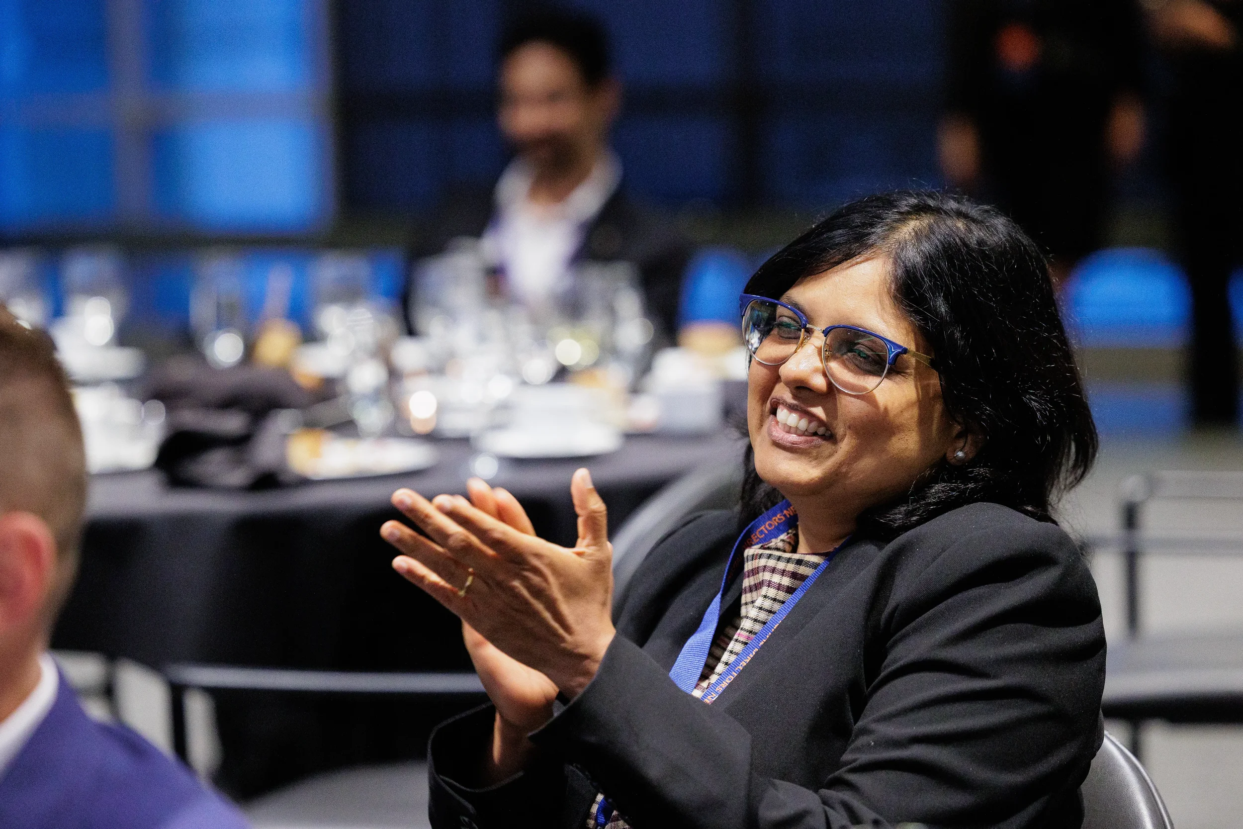 Smiling female attendee with lanyard claps while seated at dinner during Orlando corporate conference event