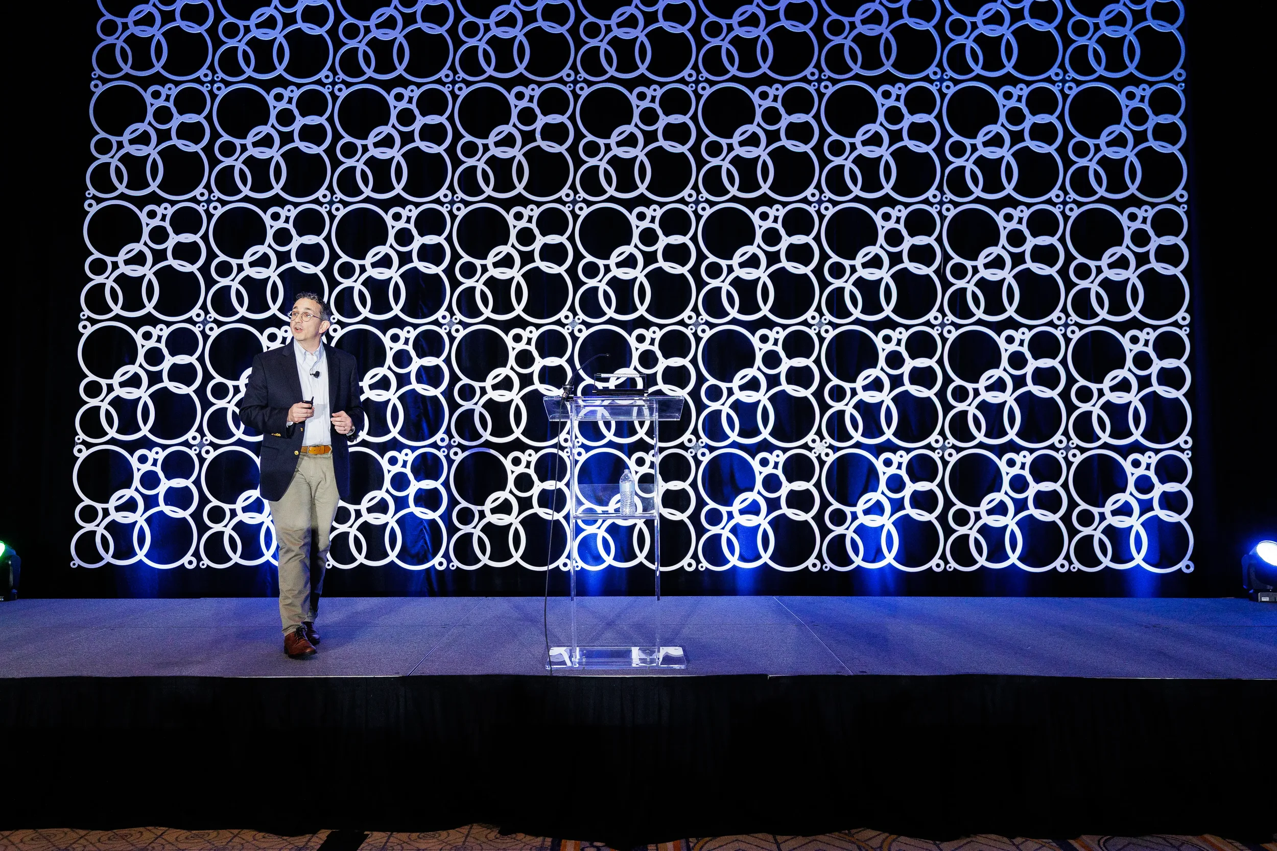 Speaker addresses audience on stage with illuminated circular backdrop at Chicago industry event