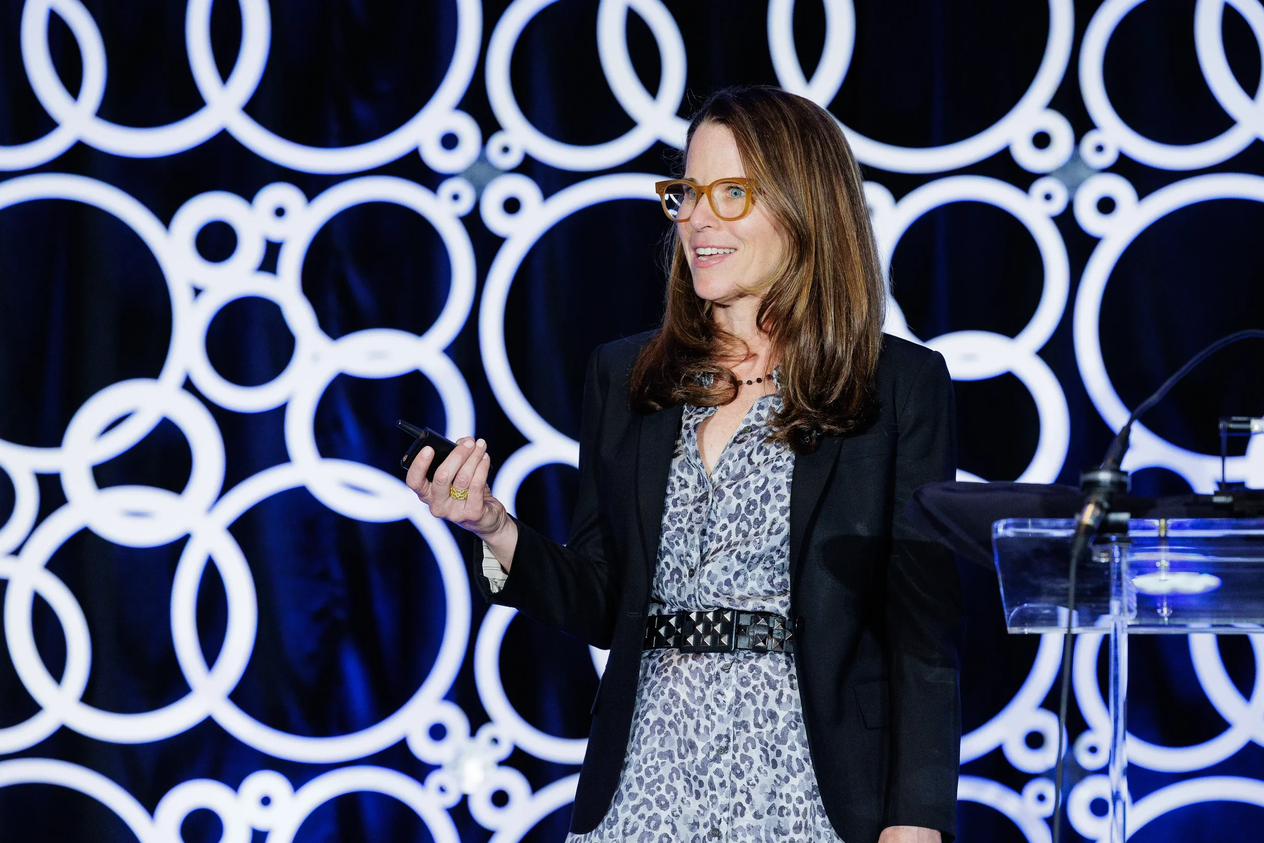 Presenter in leopard-print dress holds slide clicker on stage at Orlando industry conference