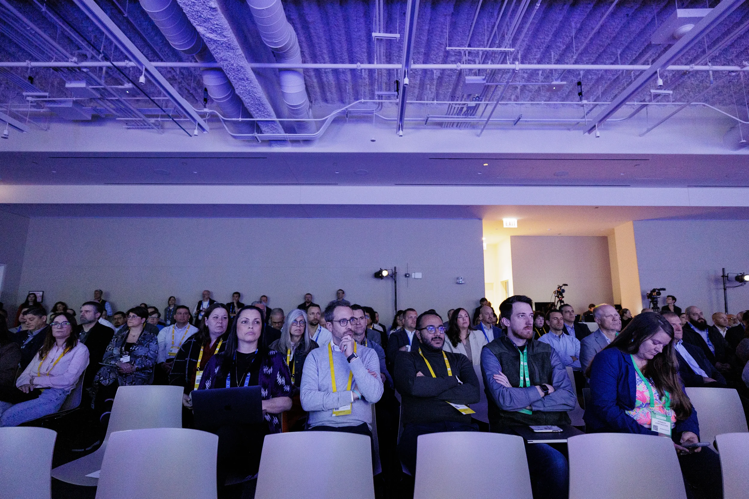 Attentive audience members with lanyards watch session in purple-lit room at Chicago industry conference