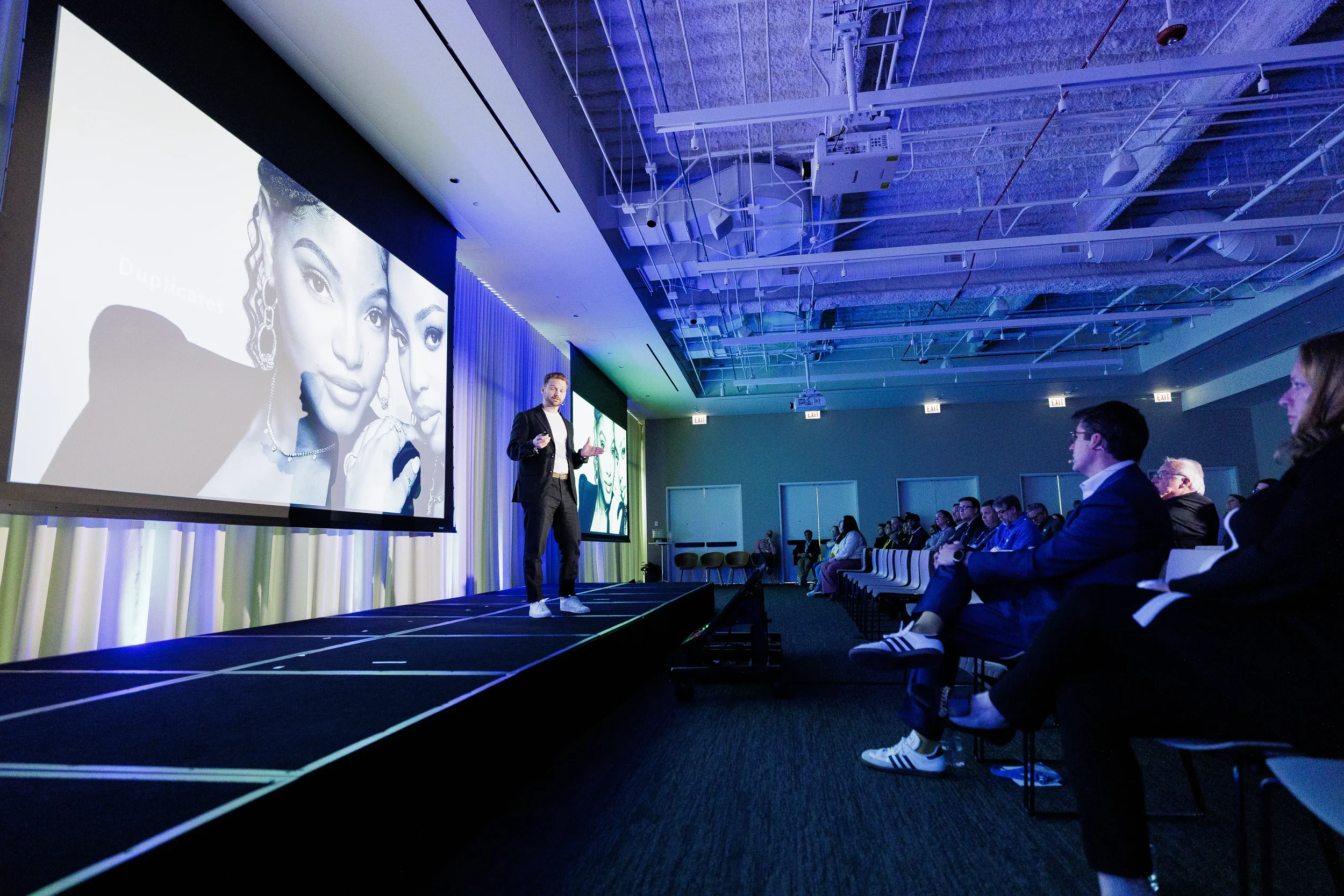 Speaker gestures on stage beside large projection screen as audience listens at Chicago industry conference