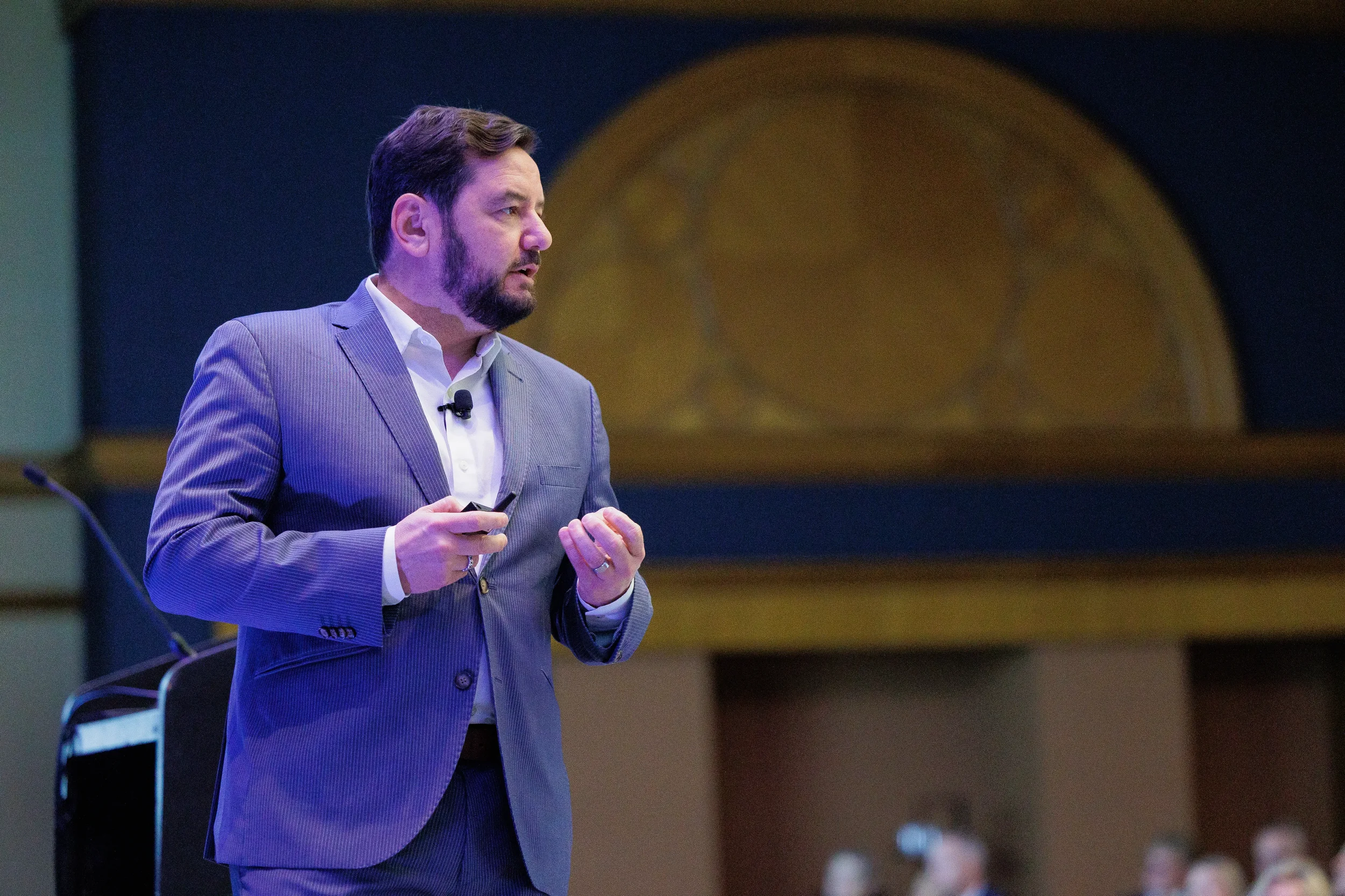 Bearded man in a blue pinstripe suit holds a remote on stage and speaks to an audience in Chicago.