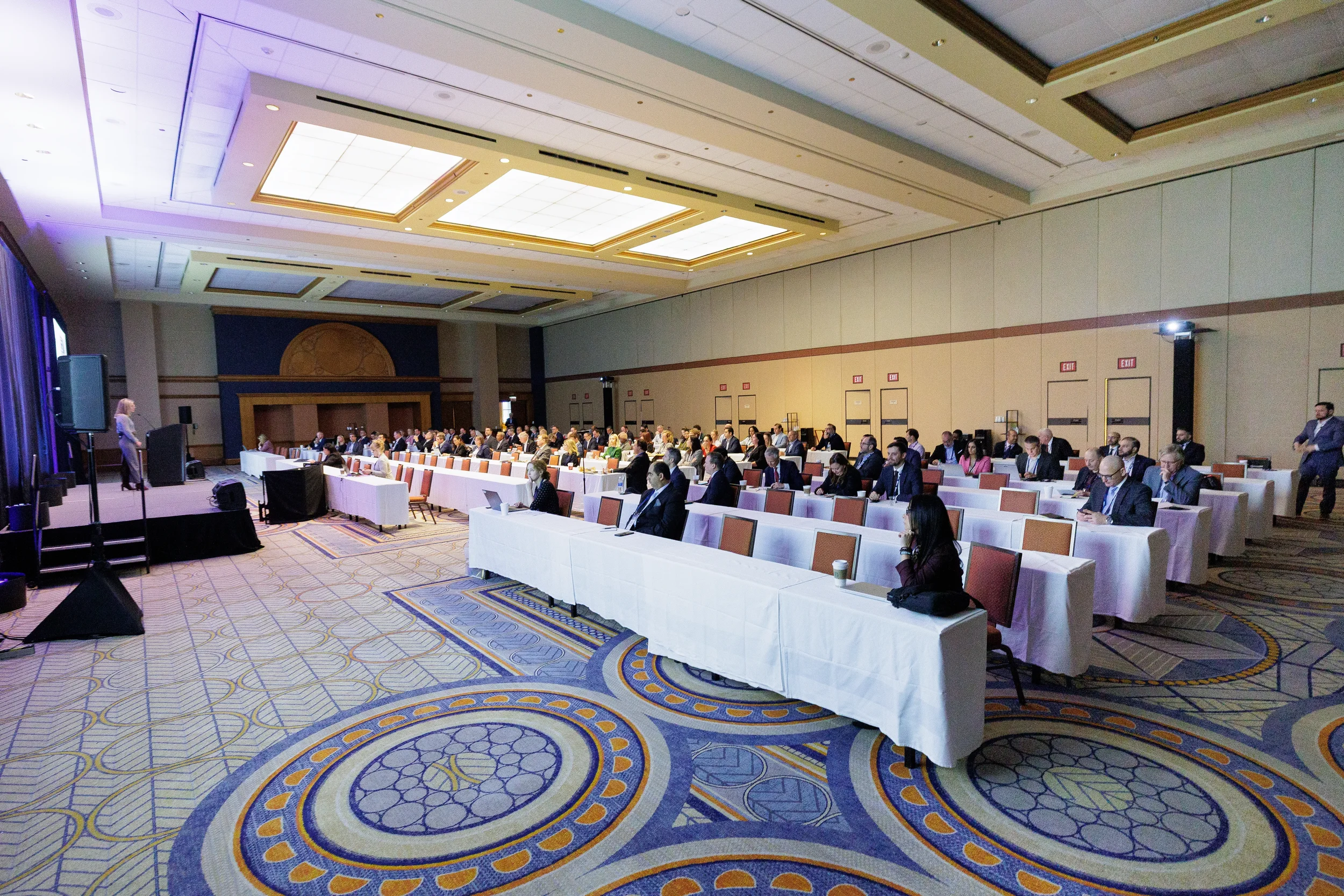 A large conference hall with attendees seated at draped tables facing a speaker on a stage in Chicago.