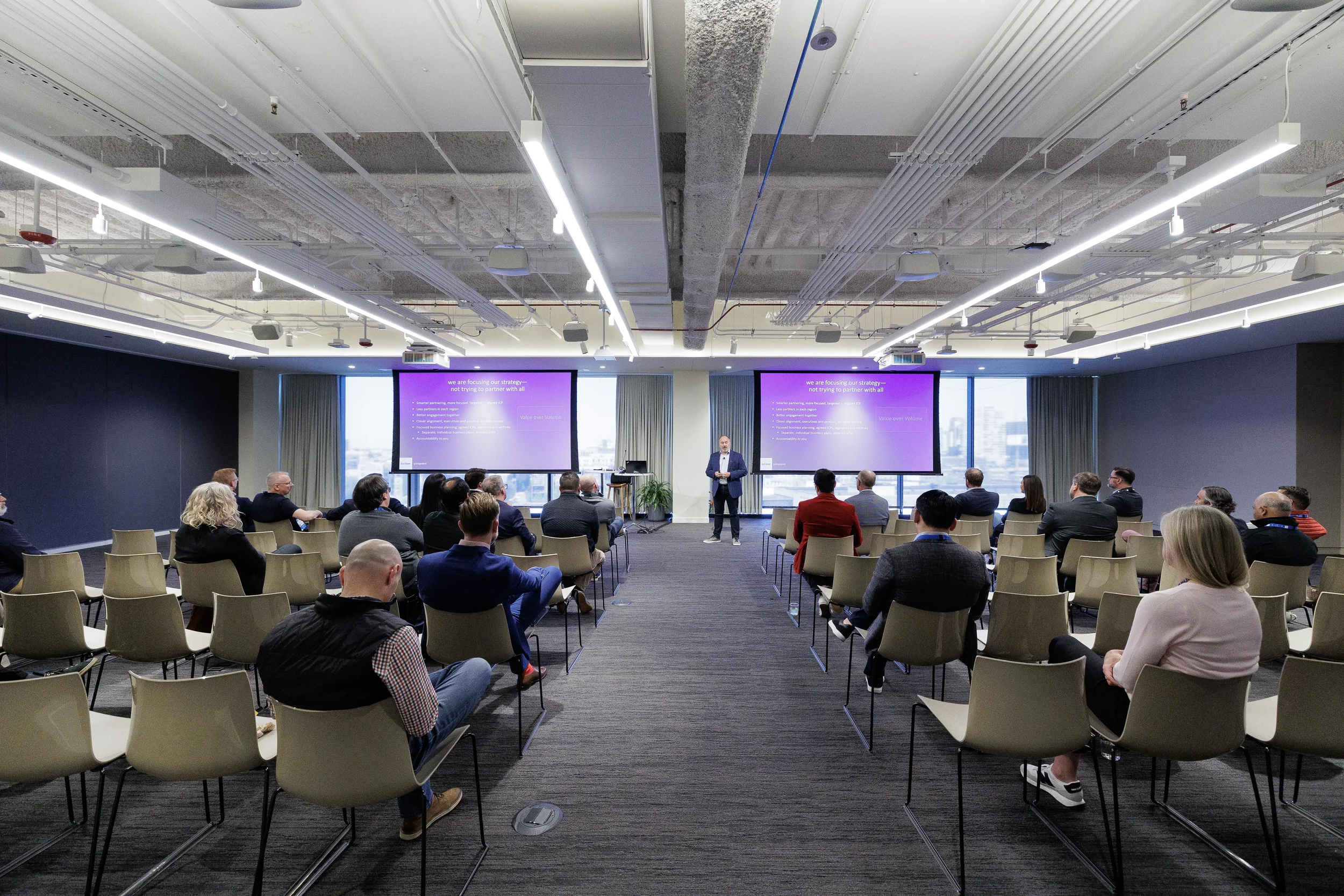 Speaker presents to seated attendees in modern meeting room with dual screens at Chicago corporate event