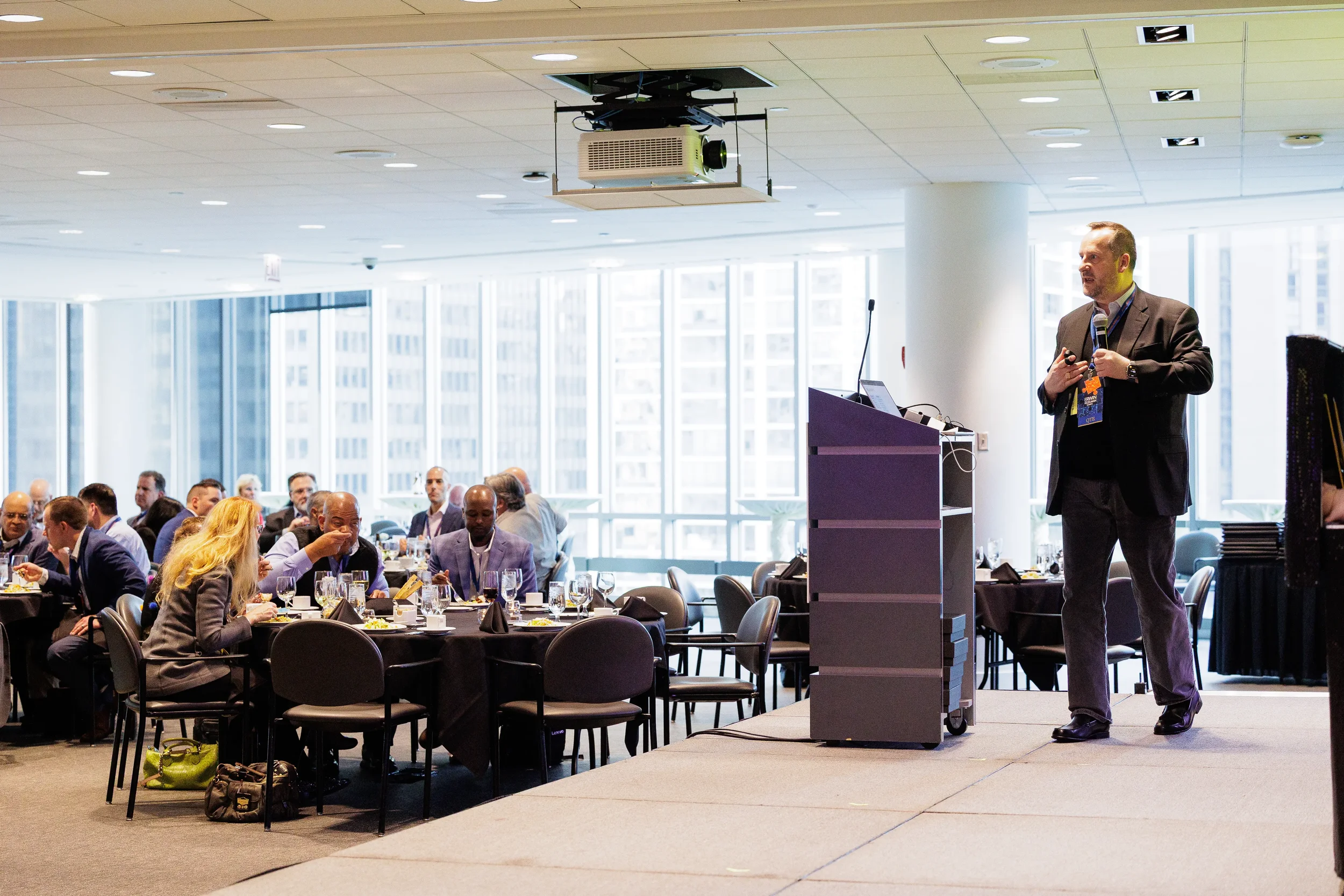 Male speaker holds microphone beside podium on stage during Orlando corporate conference luncheon session