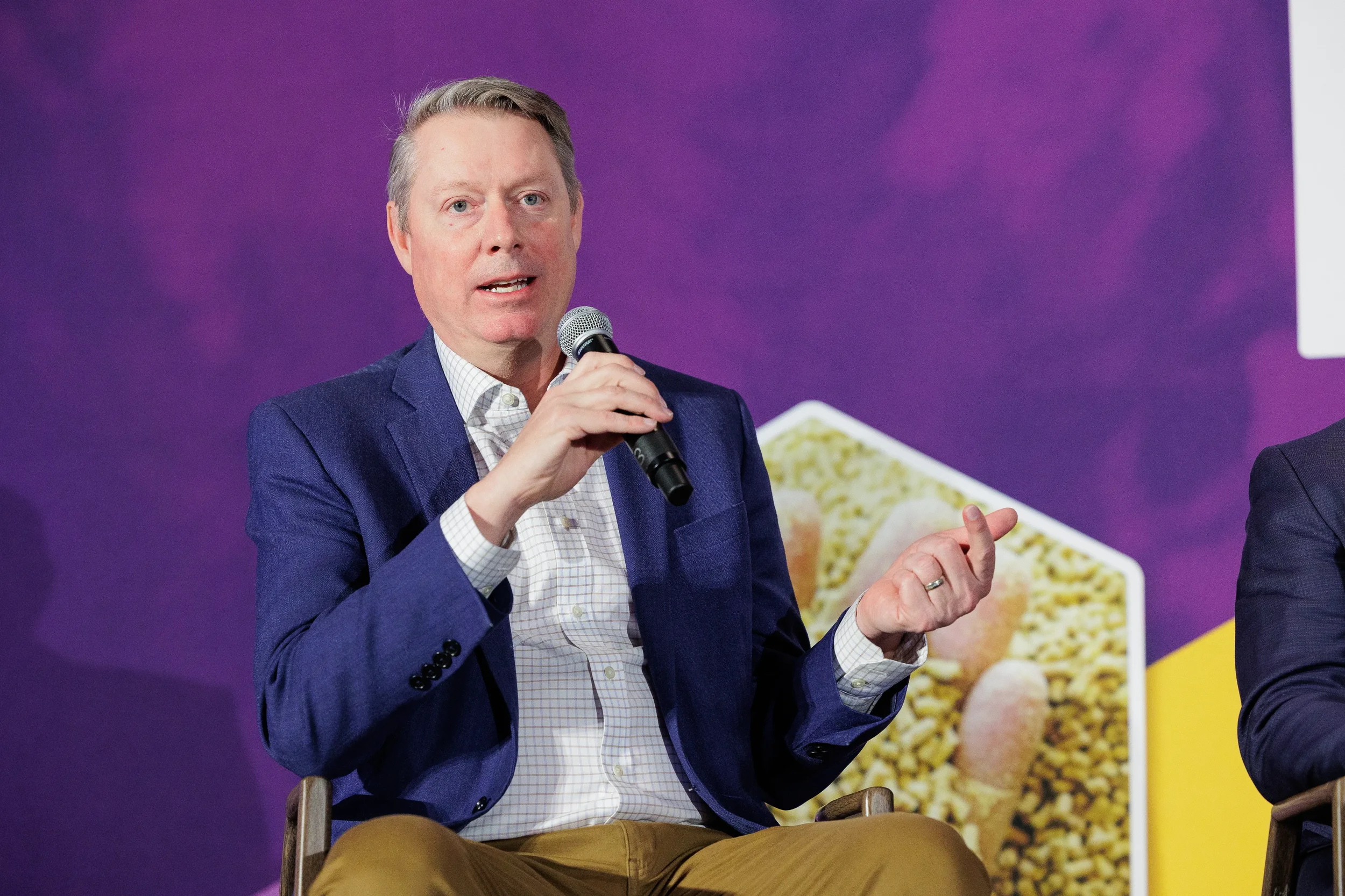 Speaker gestures while holding microphone on branded stage at Chicago industry summit